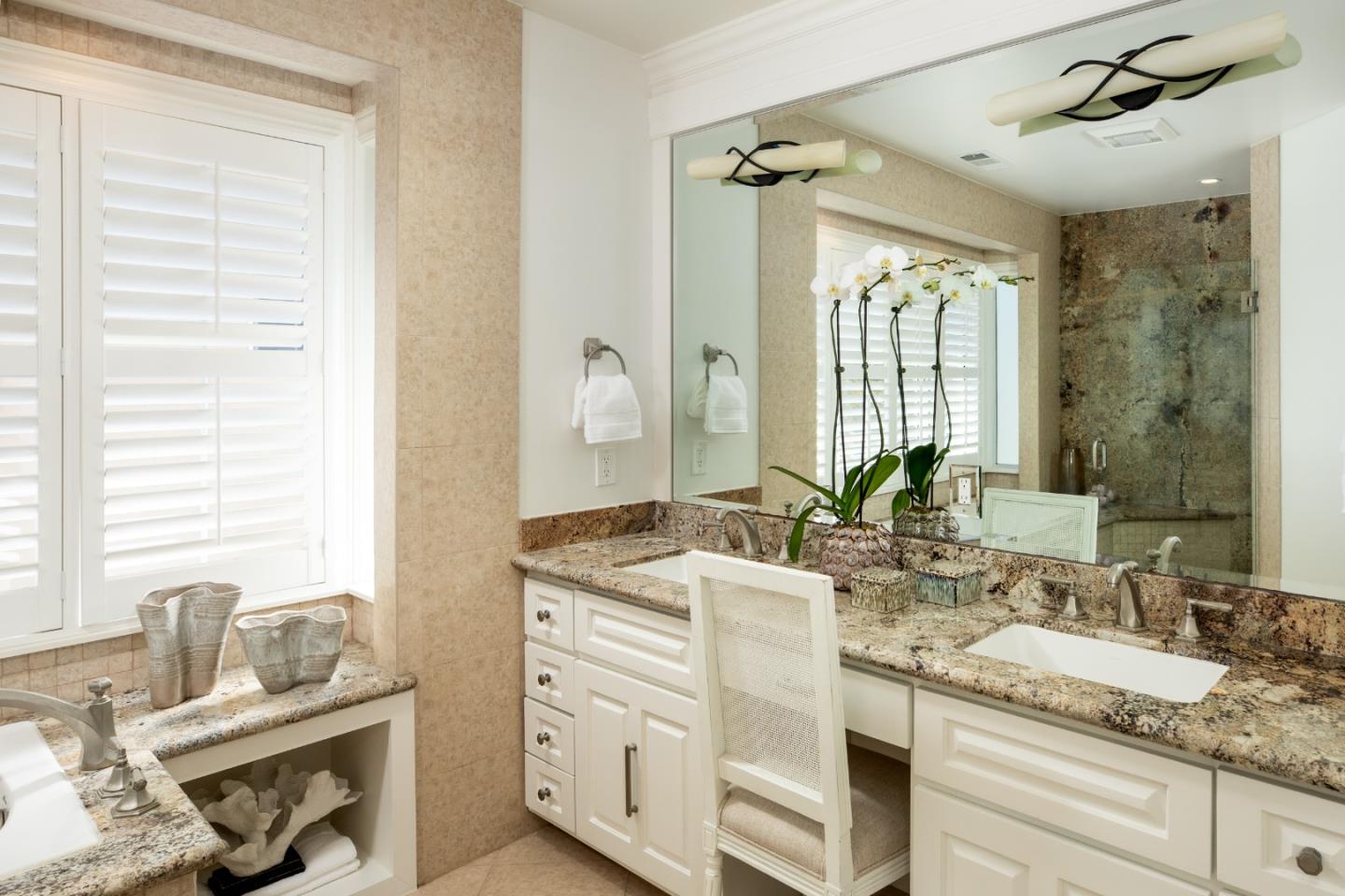 Bathroom with a granite vanity, mirrored wall, and glass-enclosed stone shower.