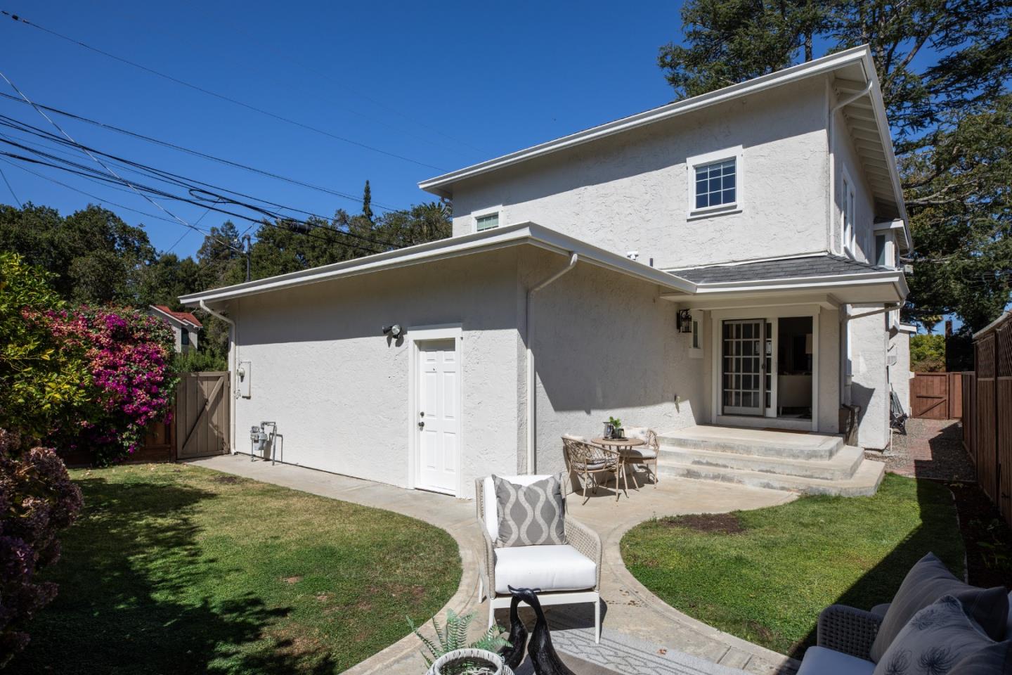 Rear of a white stucco house with a curved garden path and furnished patio.