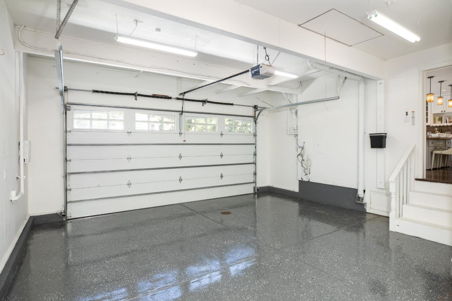 Empty garage with a polished gray floor, wide overhead door, and stairs into the house.