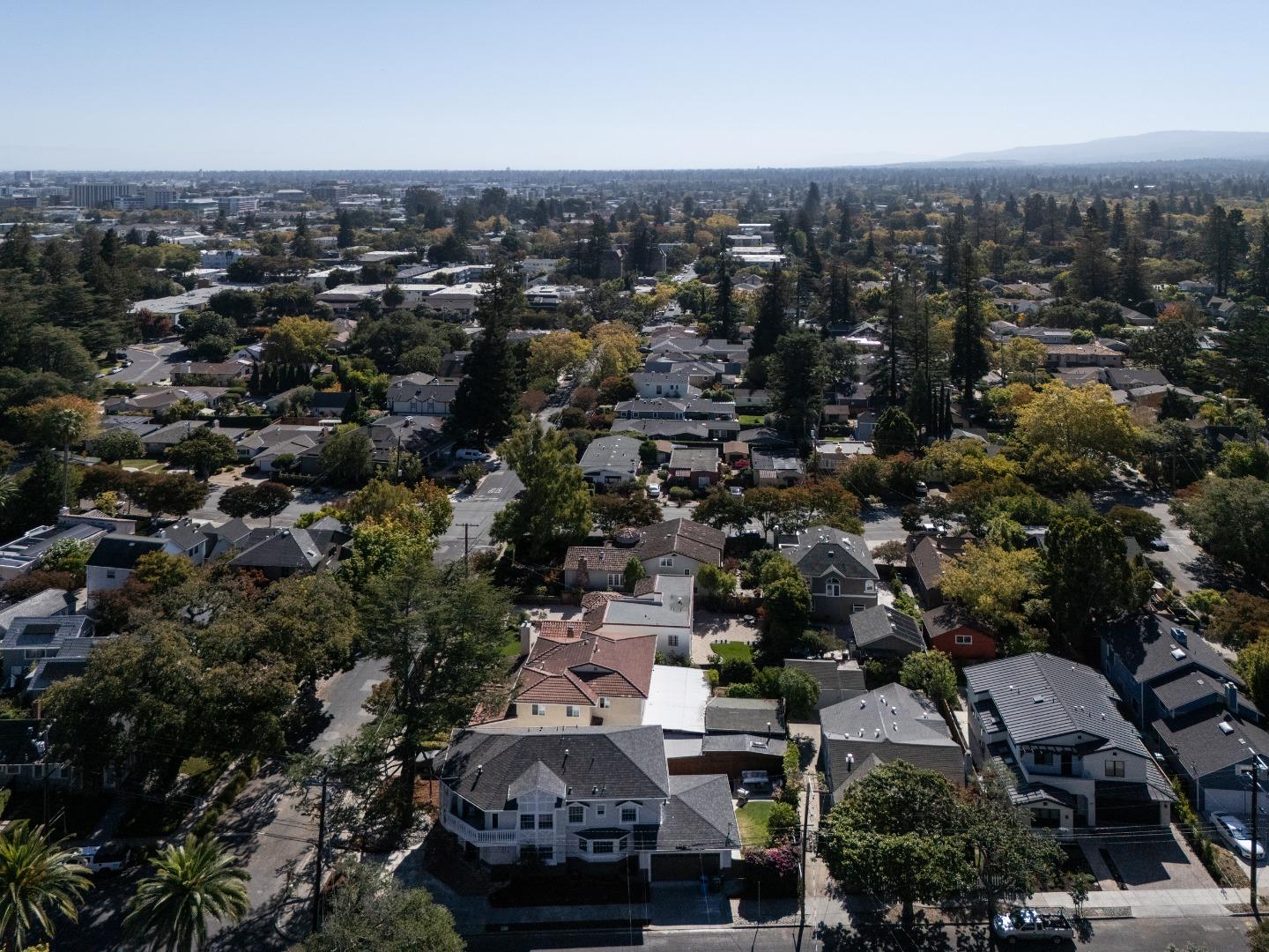 Aerial view of a leafy Redwood City neighborhood with homes, tree-lined streets, and distant hills.