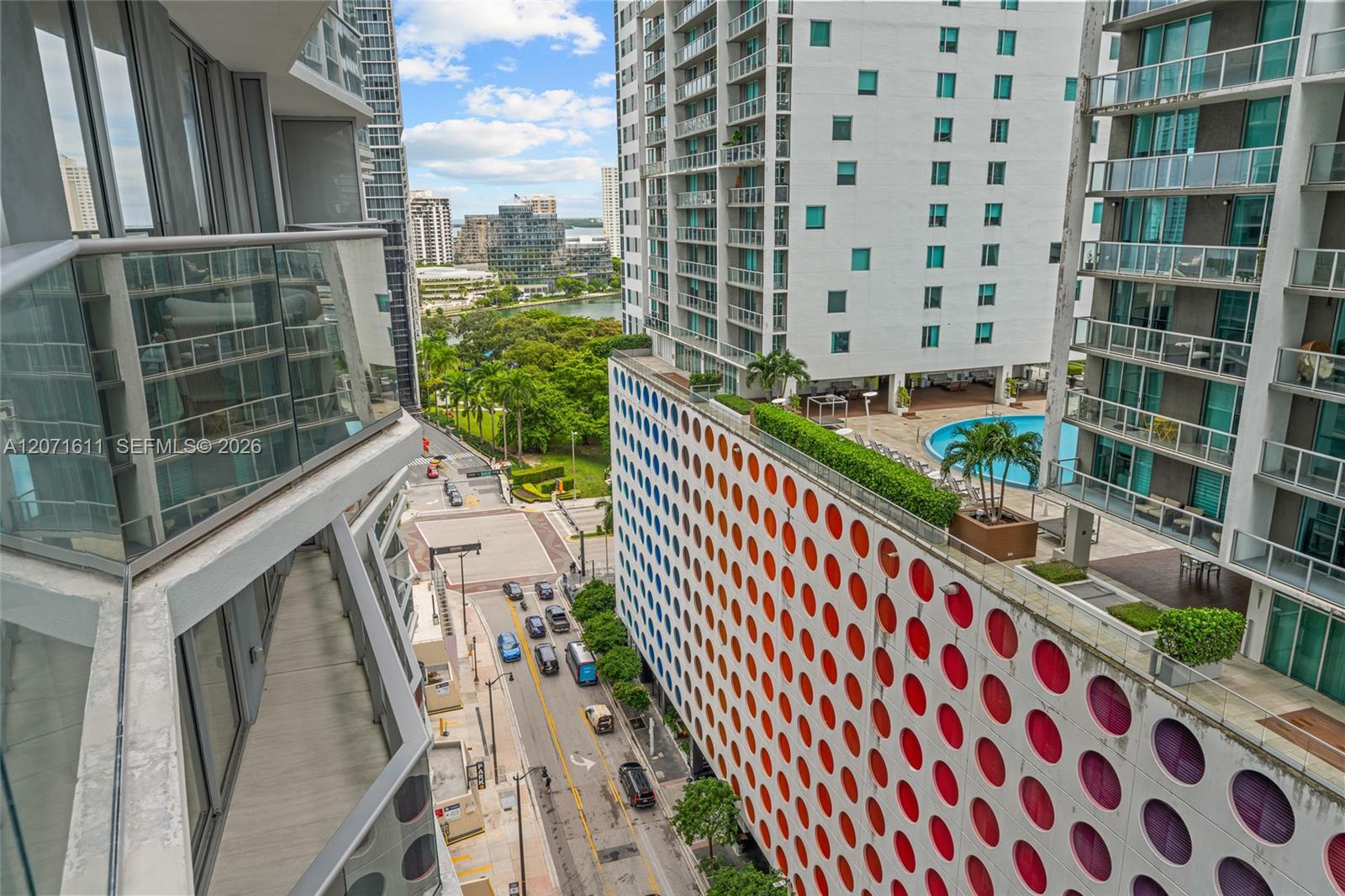 Downtown Miami view from a high-rise balcony, with neighboring towers, a rooftop pool, and colorful circular windows.