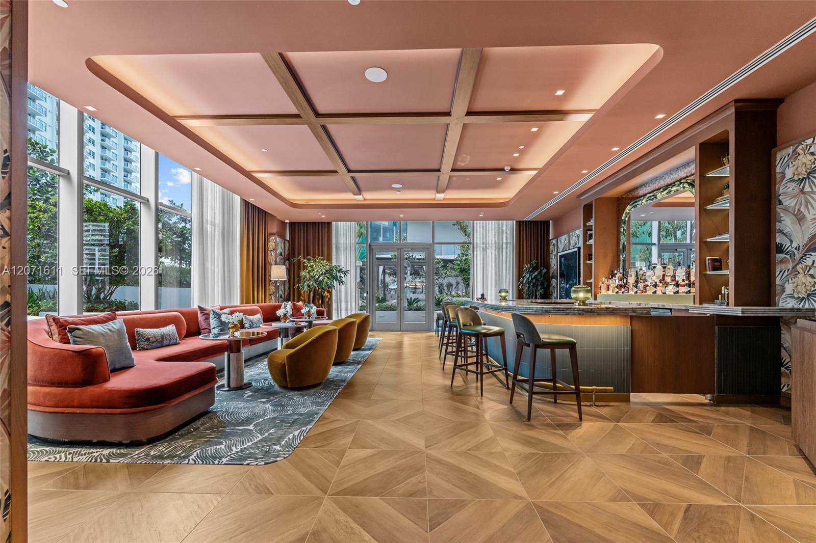 Building lounge with a coral sofa, mustard chairs, and a long bar beneath a coffered ceiling.