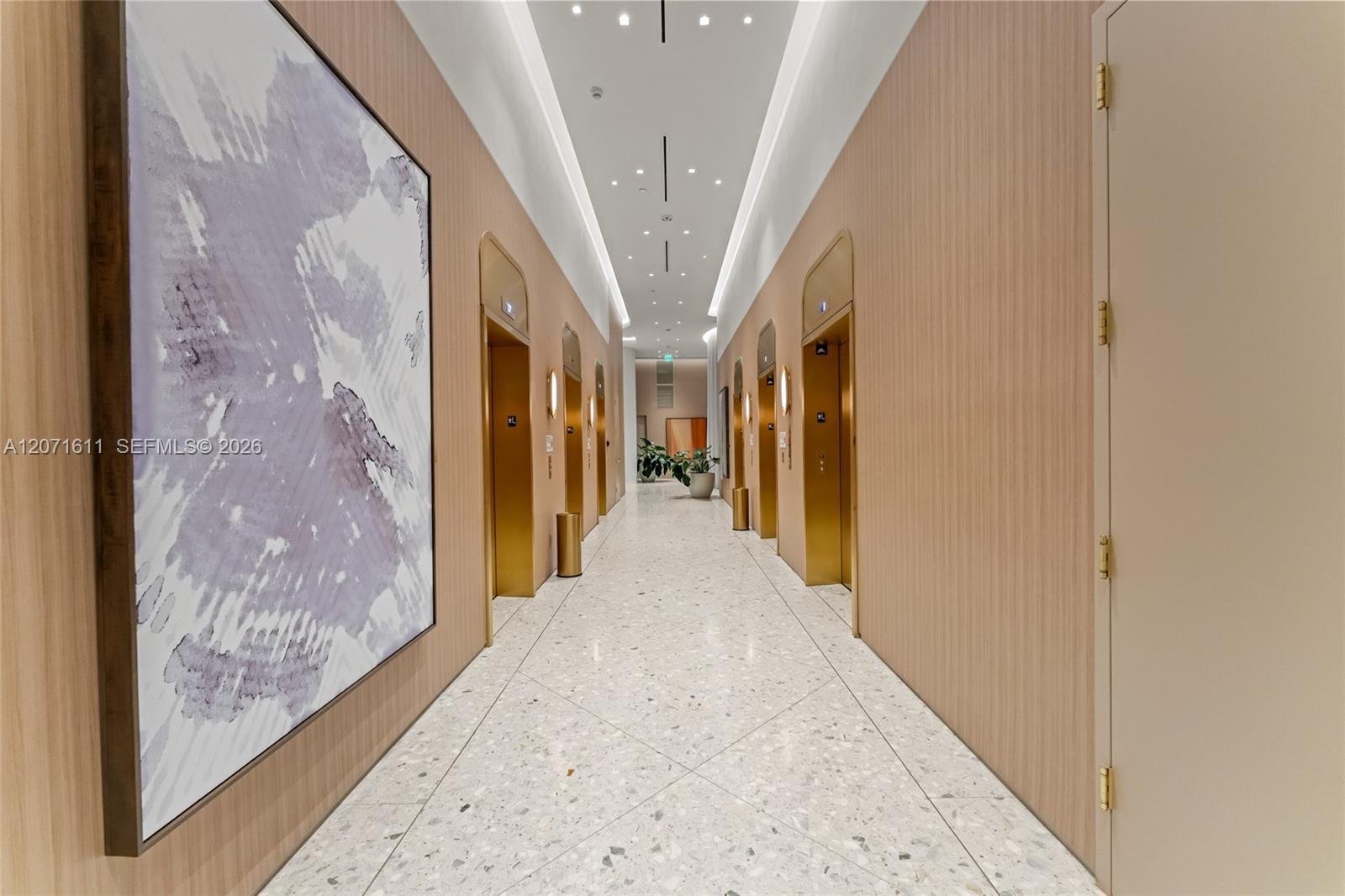 Condominium elevator hallway with gold doors, wood-paneled walls, terrazzo flooring, and large abstract artwork.