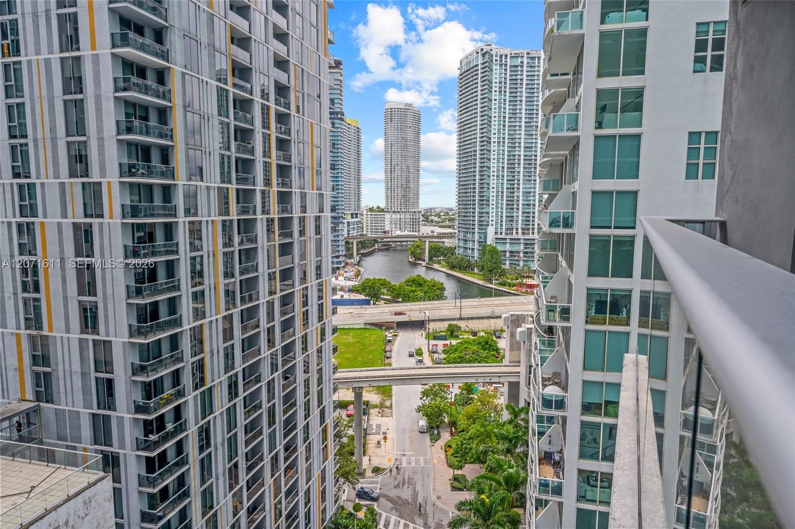 Miami high-rise view from a balcony, with the river and neighboring towers in the distance.