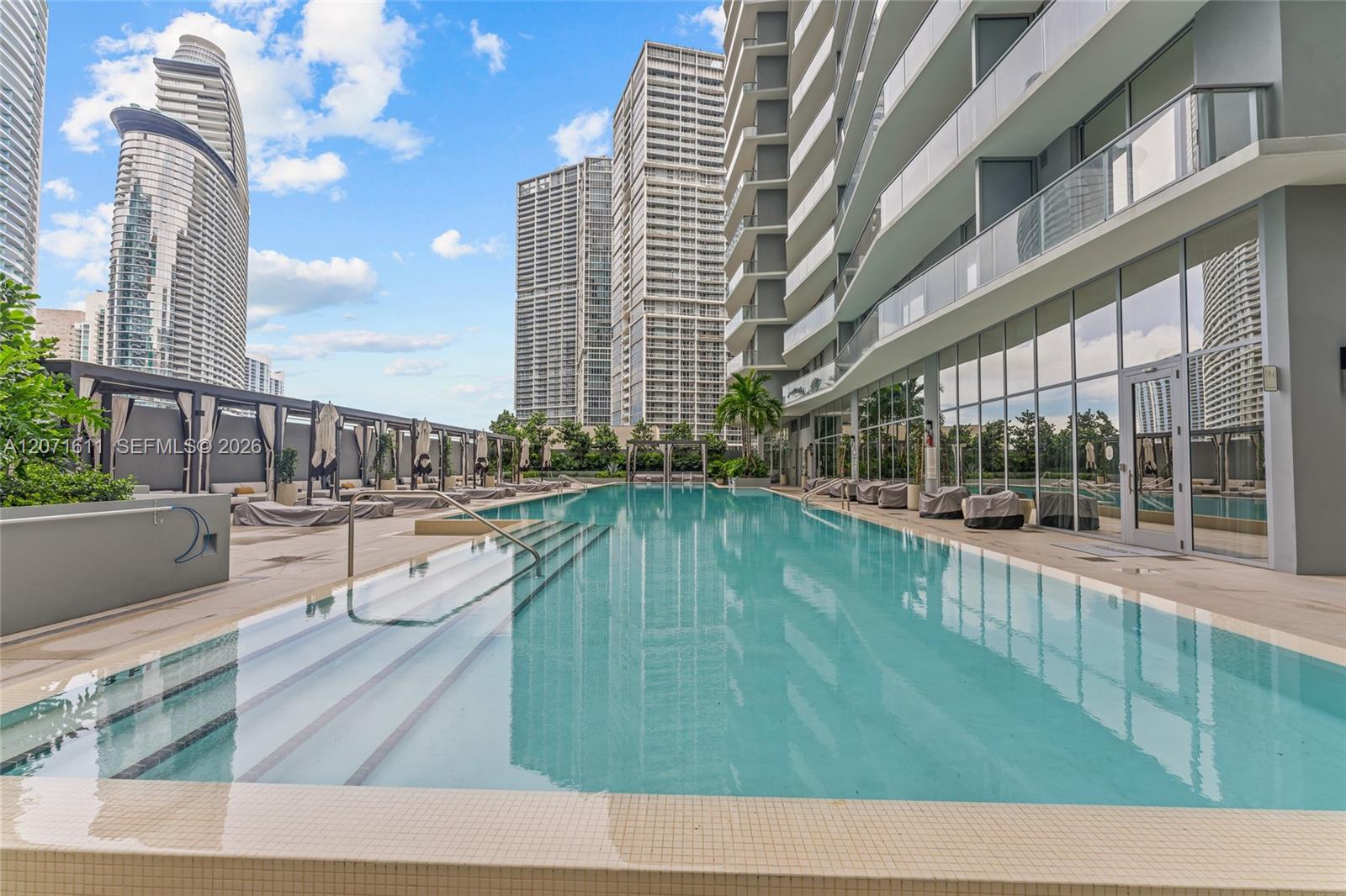 Outdoor condominium pool with broad entry steps, cabanas, and Miami high-rises in the background.