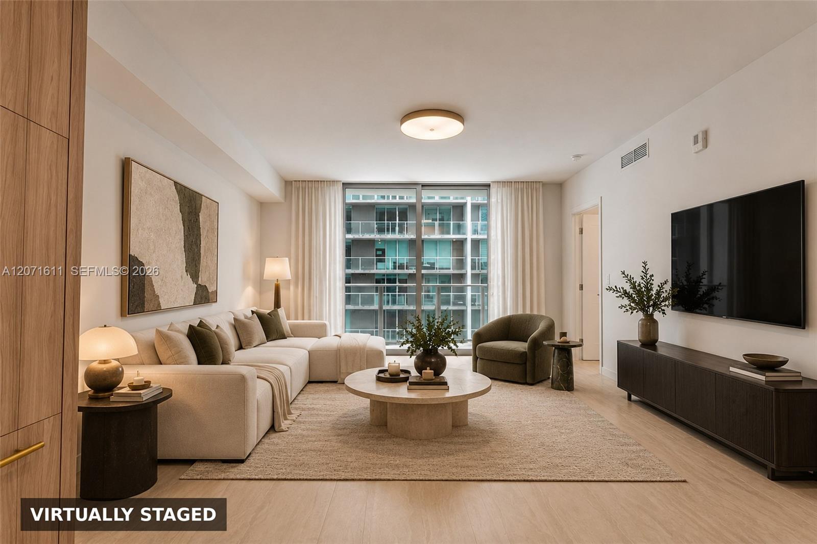 Virtually staged condominium living room with a cream sectional and large window overlooking a neighboring high-rise.