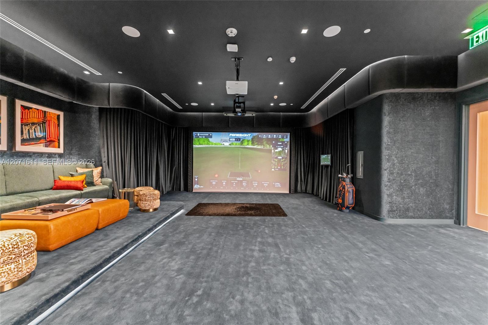 Furnished golf simulator lounge with a large projection screen, sectional seating, and golf clubs.