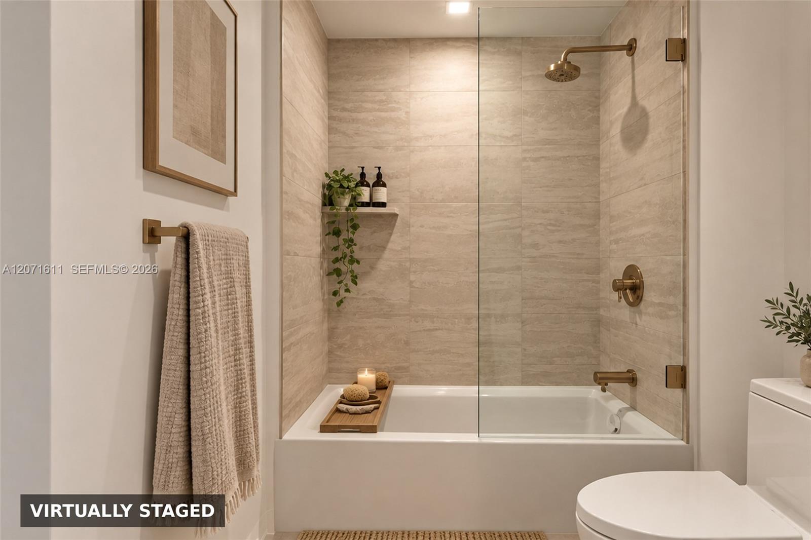 Bathroom with a glass-enclosed tub, beige tile, brass fixtures, and a towel.