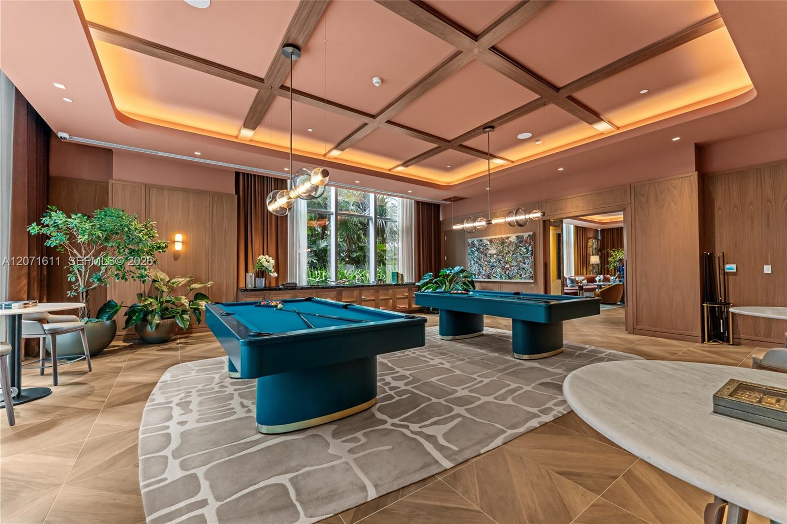 Residents’ billiards room with two teal pool tables and large windows overlooking greenery.