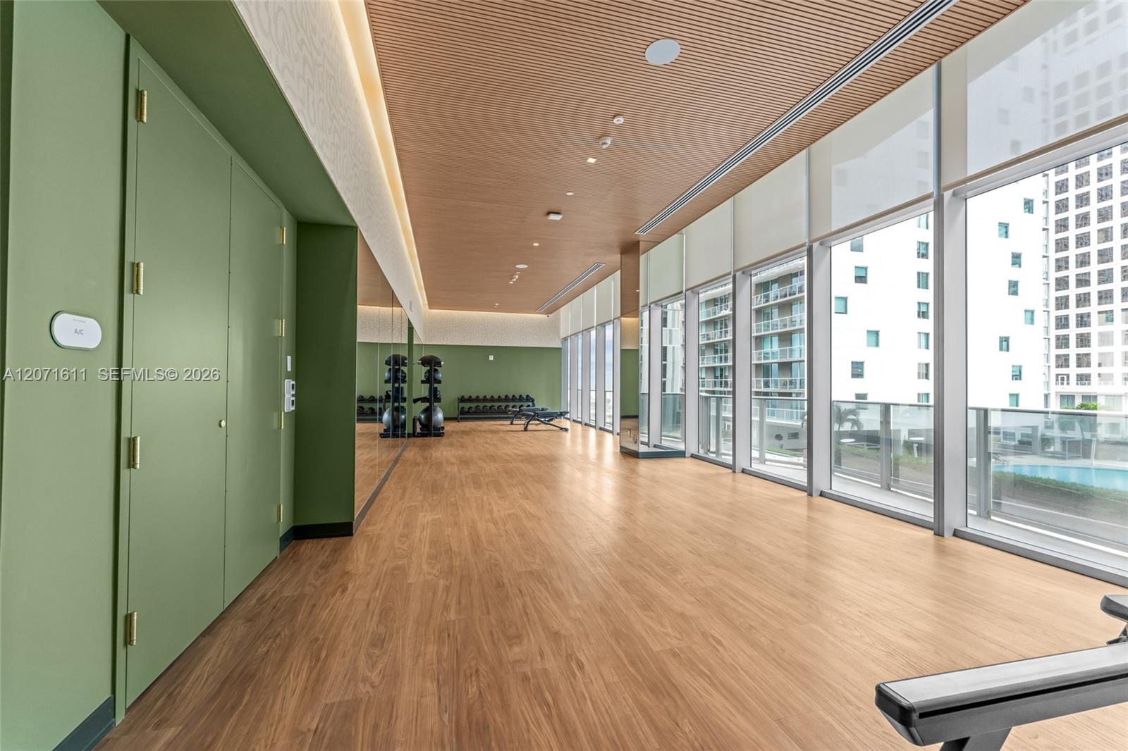Condominium fitness room with mirrored walls, exercise equipment, and floor-to-ceiling windows.