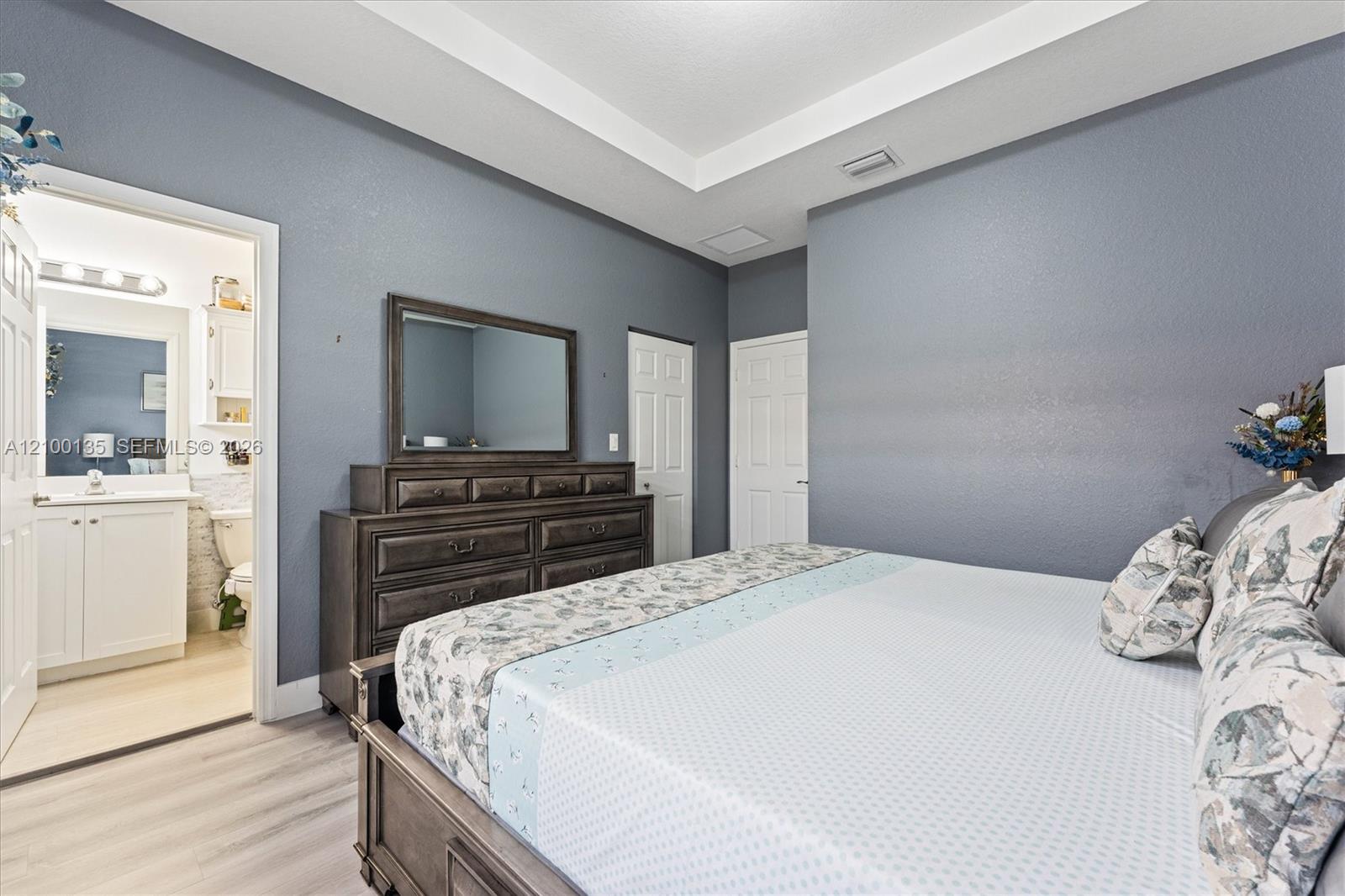 Furnished bedroom with a large bed and dark wood dresser; attached bathroom visible through the doorway.