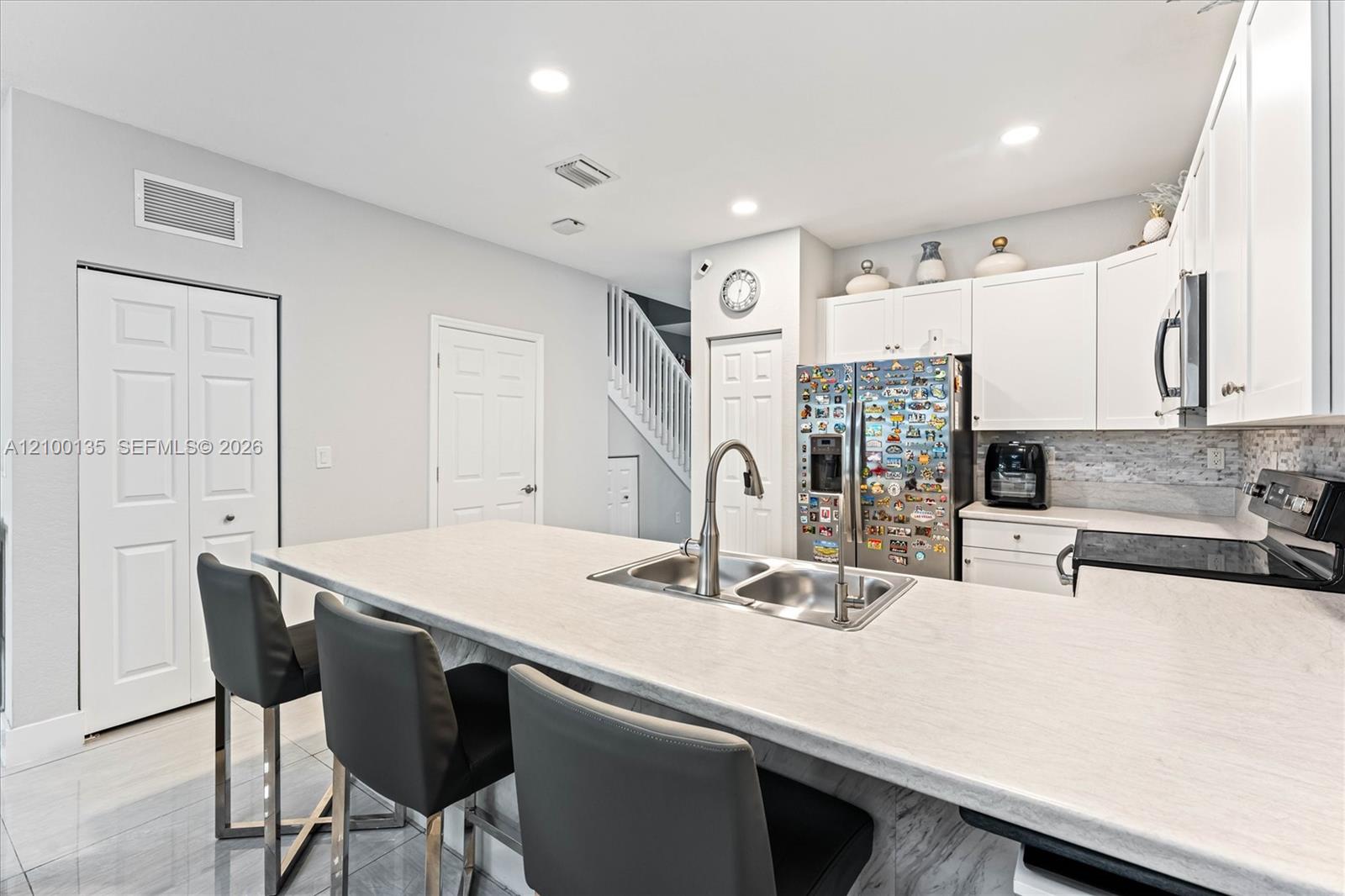 Modern kitchen with white cabinetry, a large island, double sink, and dark bar stools.