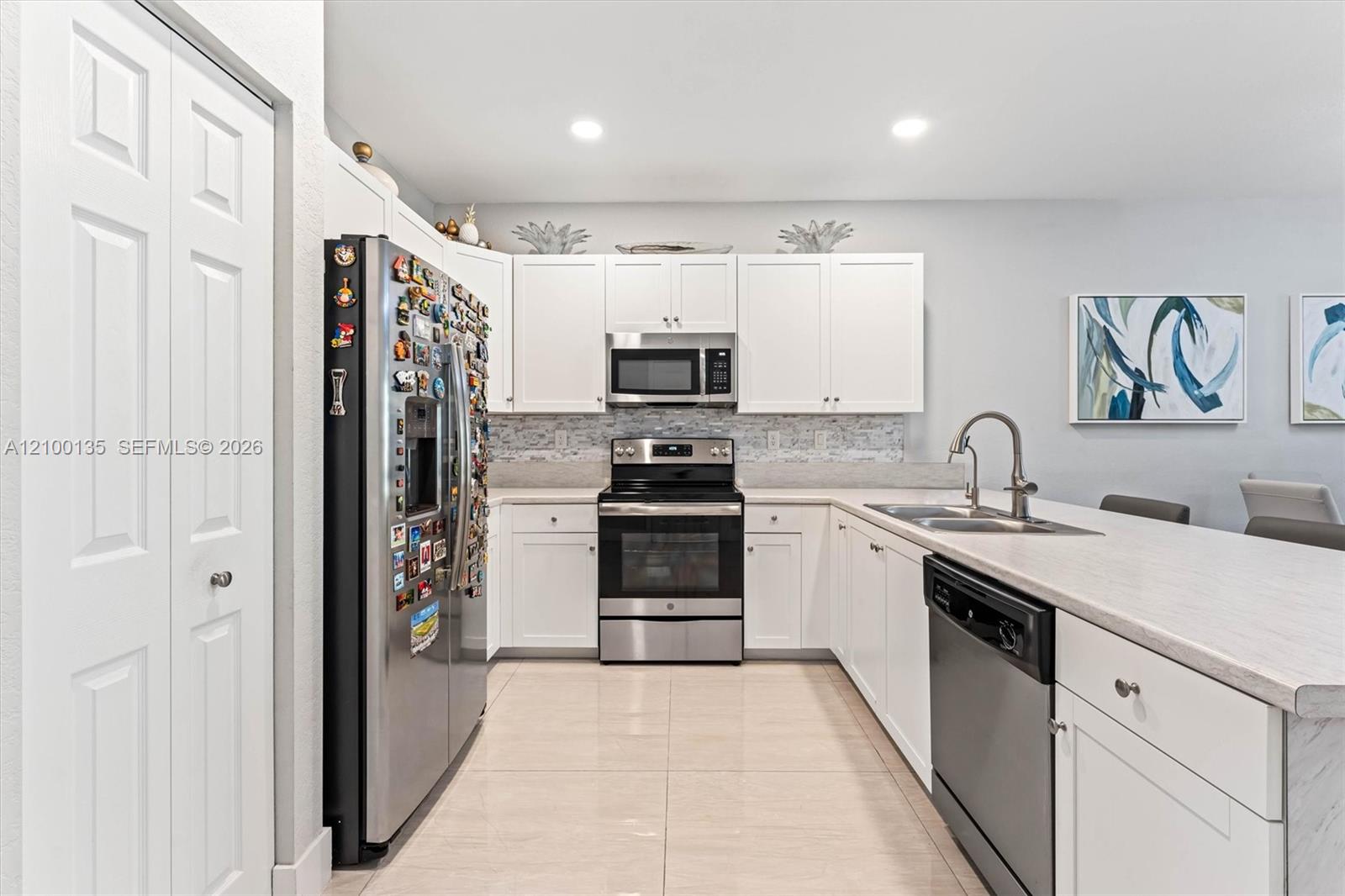 Kitchen with white cabinets, stainless steel appliances, gray tile backsplash, and a long sink peninsula.