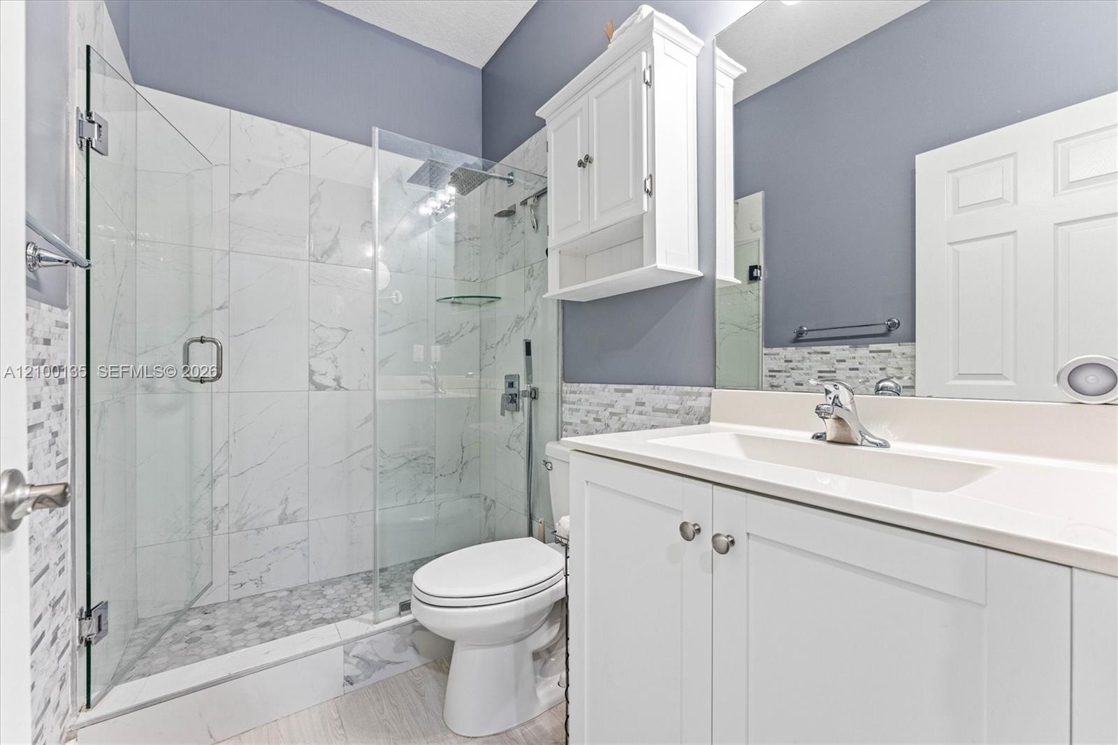 Bathroom with a glass walk-in shower, marble-look tile, and white vanity.