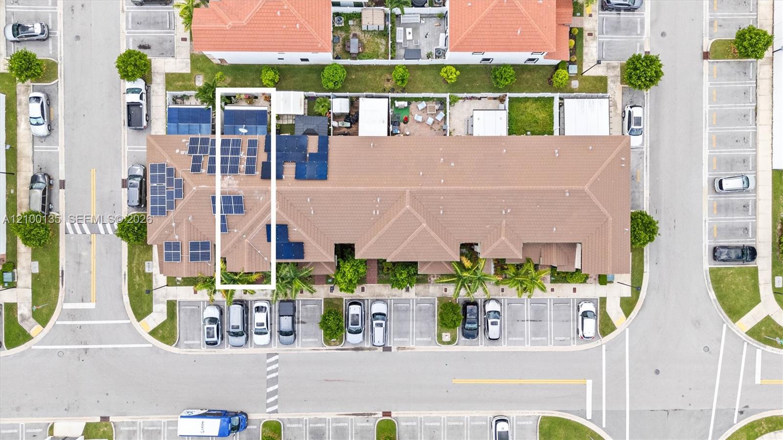 Aerial townhouse complex with one unit outlined in white and solar panels on nearby roofs.