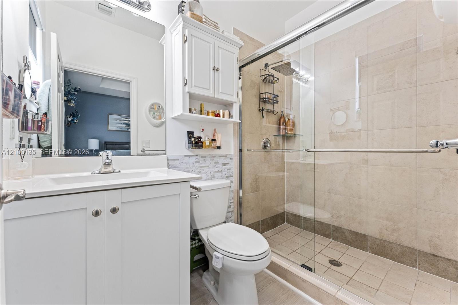 Bathroom with a white vanity and toilet beside a large beige-tiled glass shower.