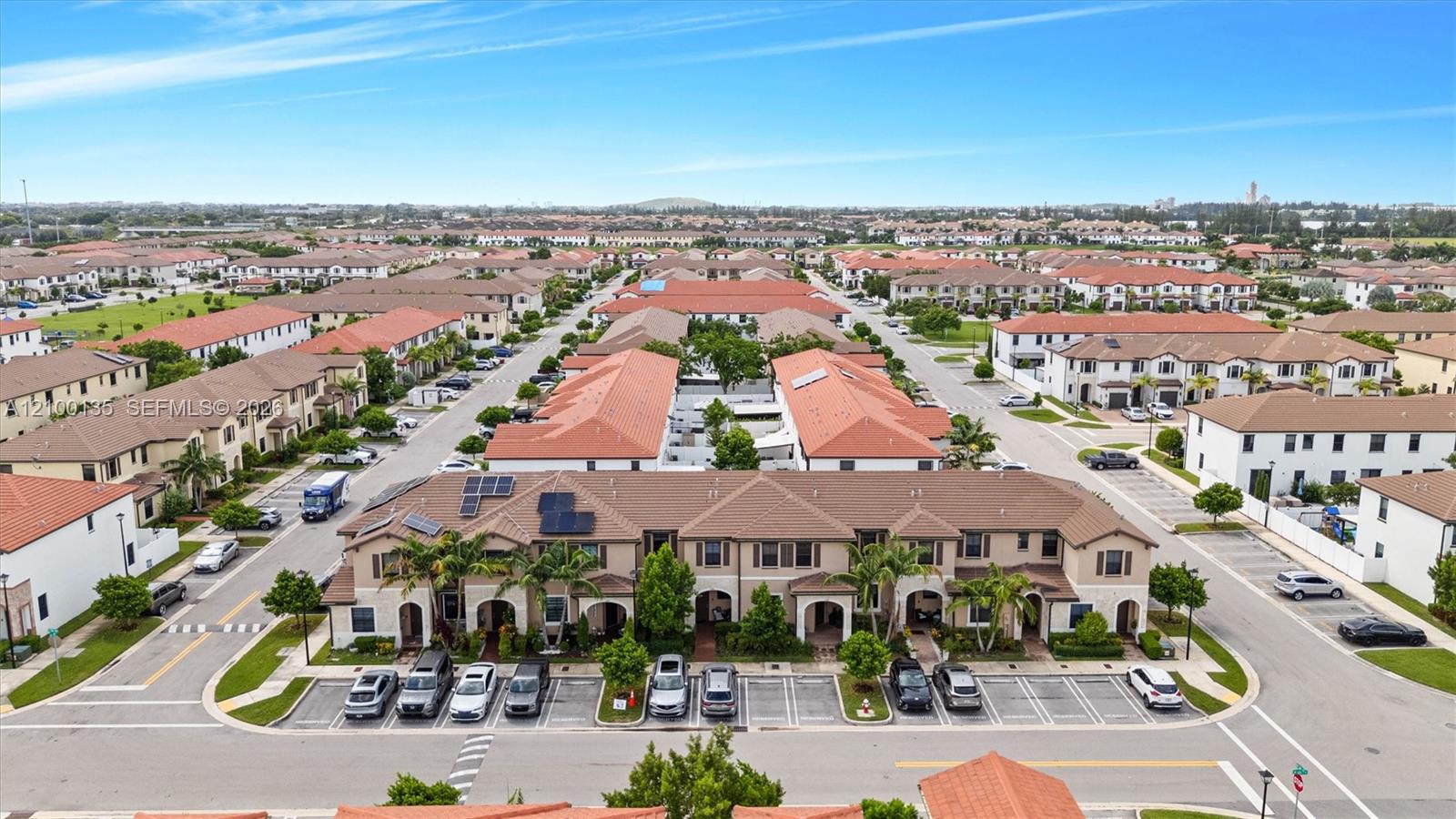 Aerial view of a townhome community with tile roofs, parking, and intersecting streets.