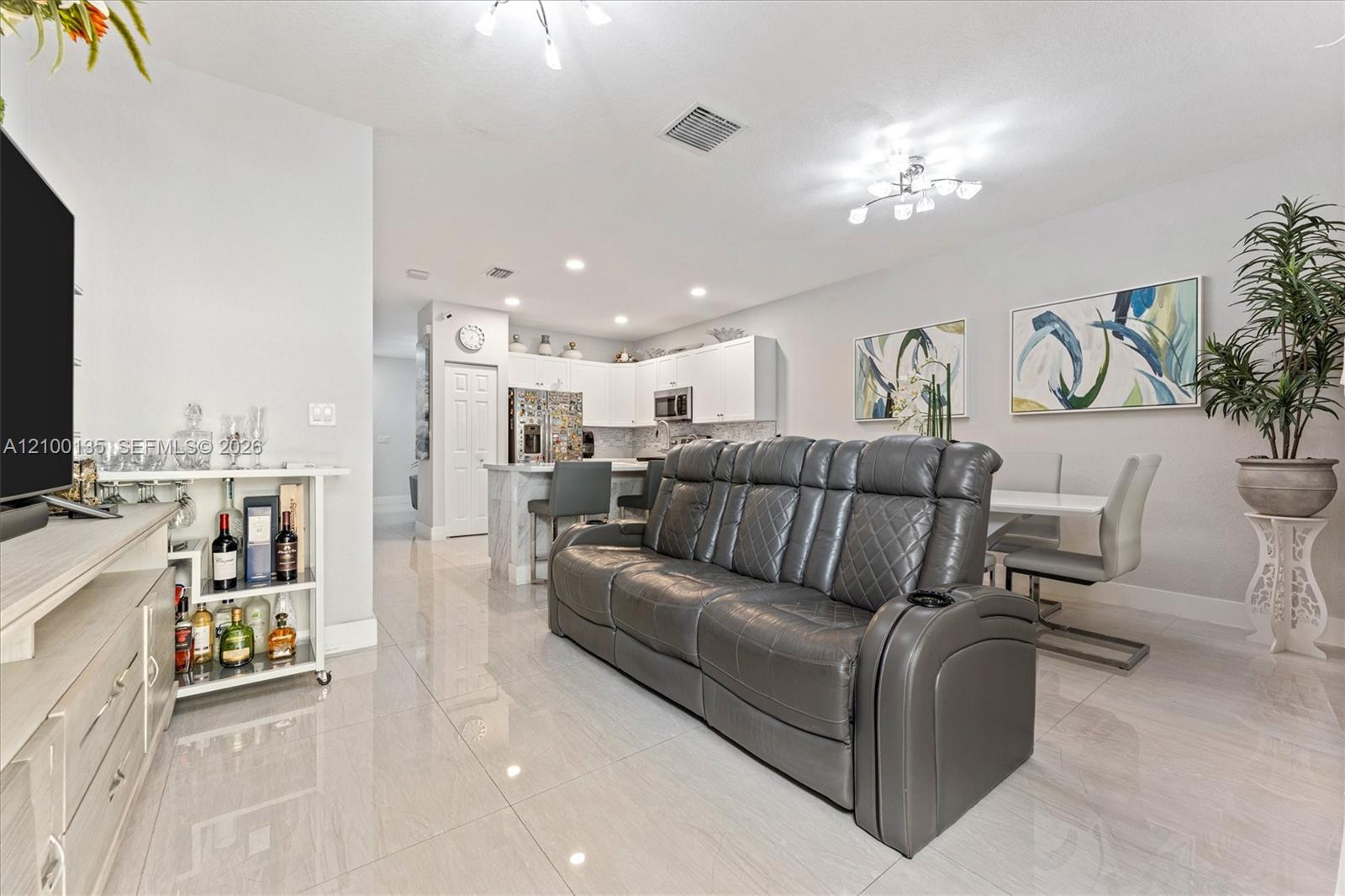 Open-plan living room with gray leather reclining sofa, dining area, and white kitchen.