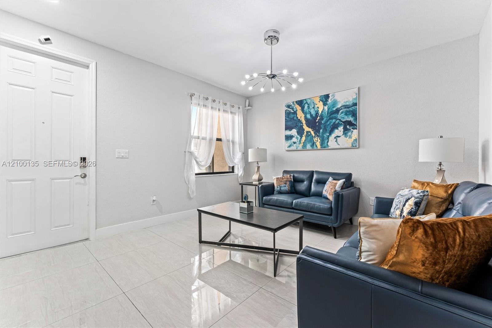 Staged living room with blue leather sofas, glossy tile floors, and abstract blue wall art.