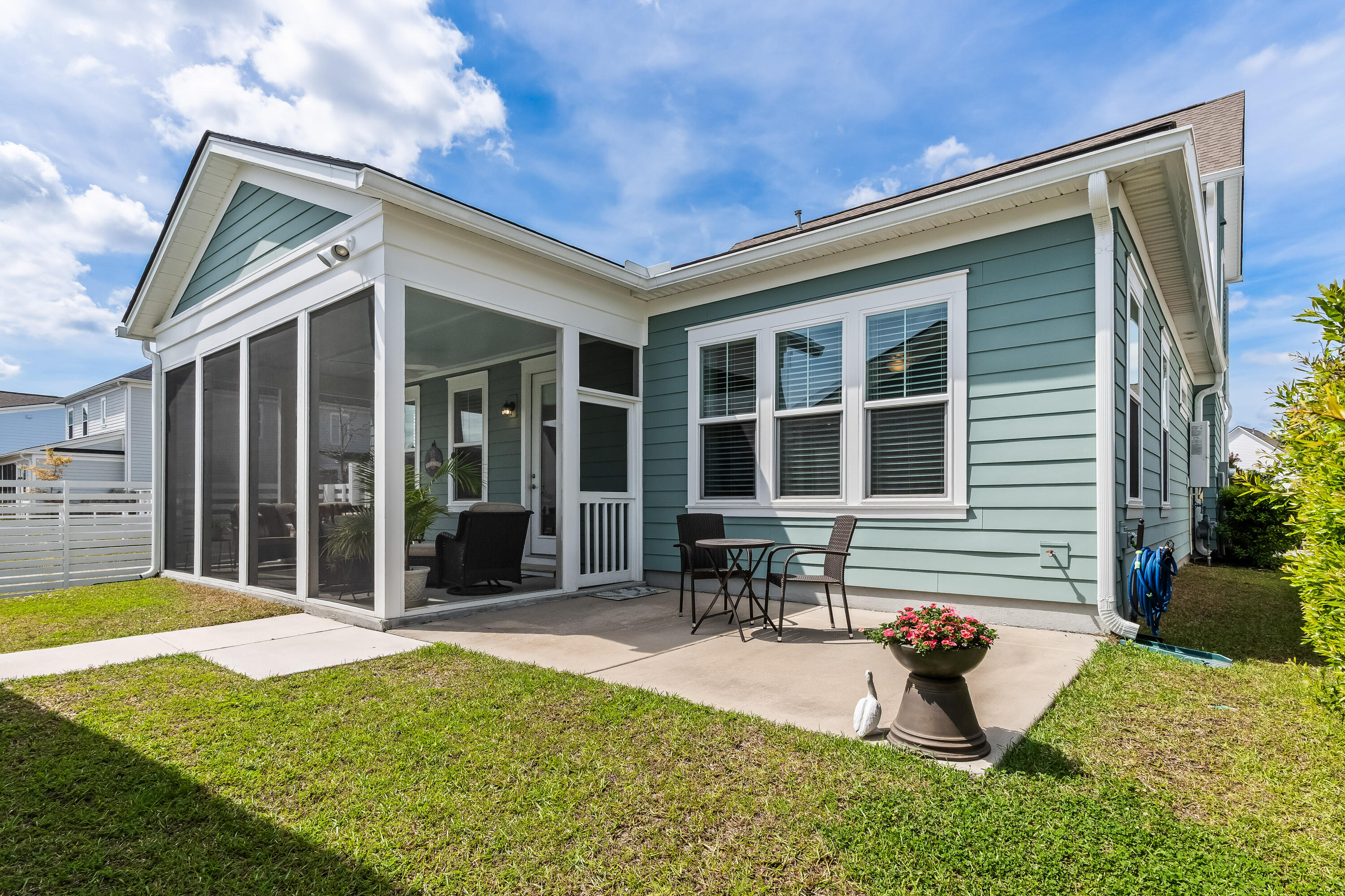 Home’s pale blue-green rear exterior with a screened porch and furnished patio beside the lawn.