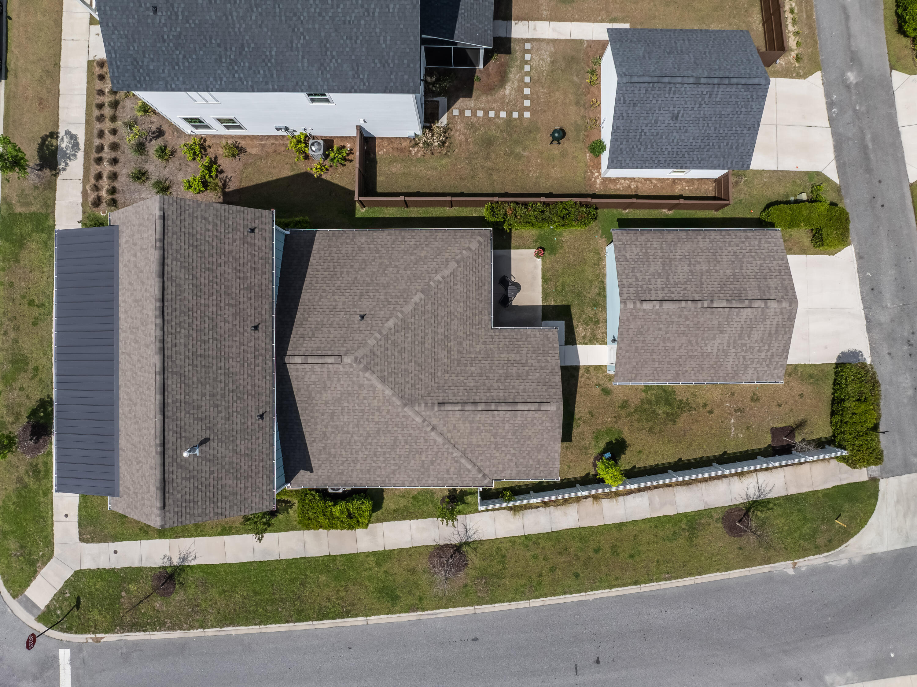 Aerial view of a gray-roofed home on a corner lot with a fenced backyard.