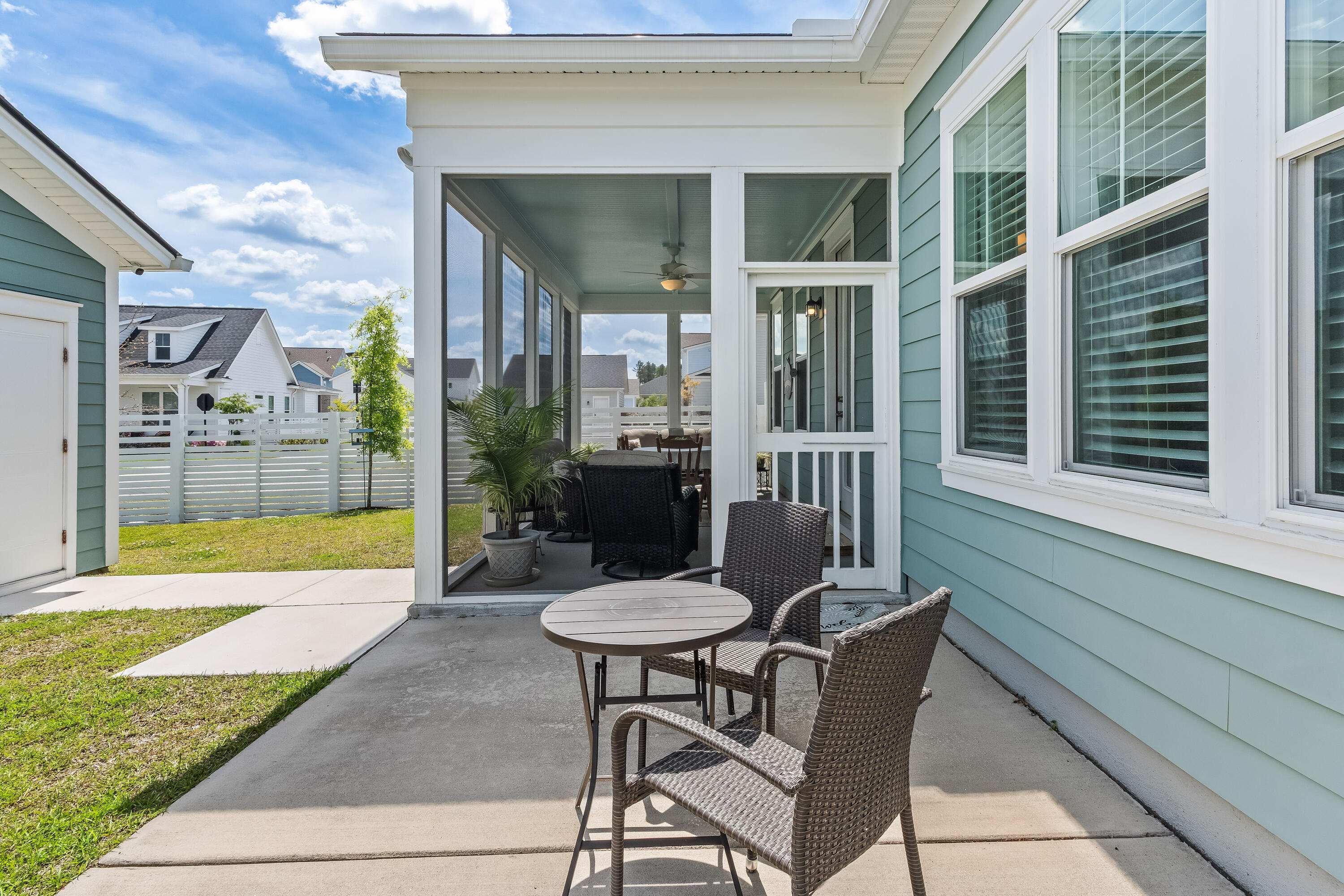 Patio with wicker chairs and table beside a screened porch and fenced lawn.