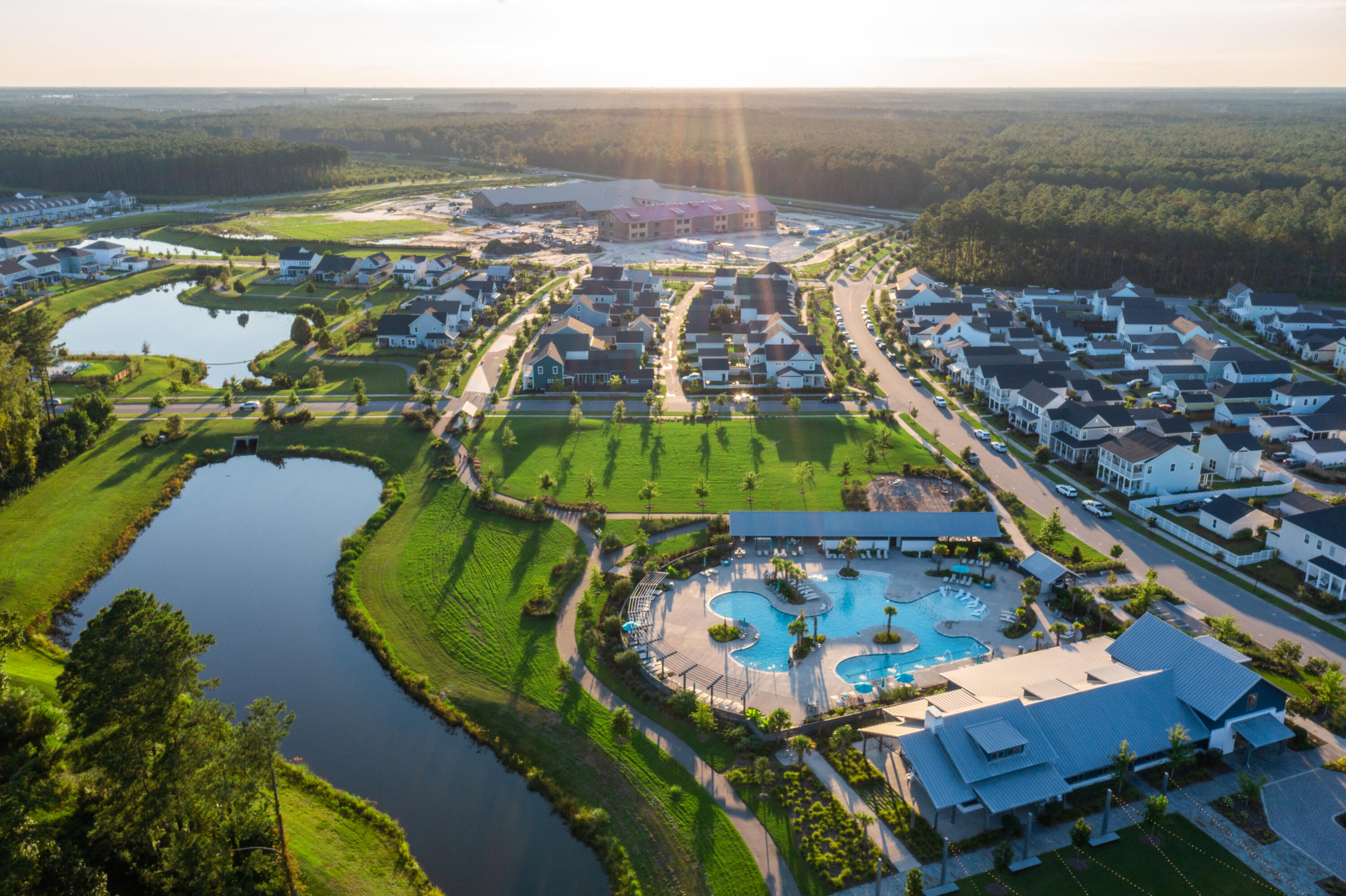 Aerial view of a neighborhood with a resort-style pool, ponds, and clubhouse at golden hour.