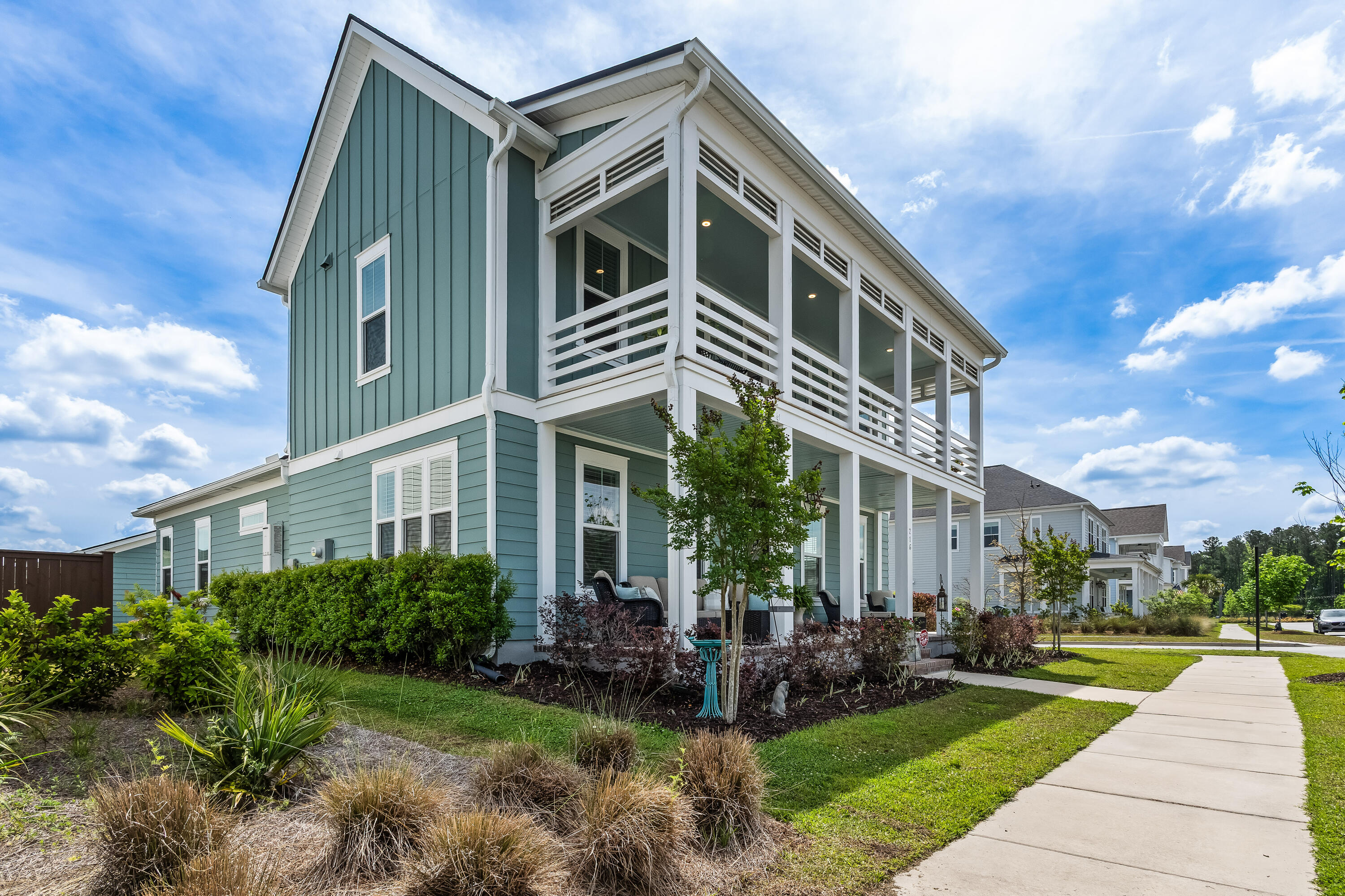 Blue-green two-story home with white trim, covered upper porch, and landscaped front yard.
