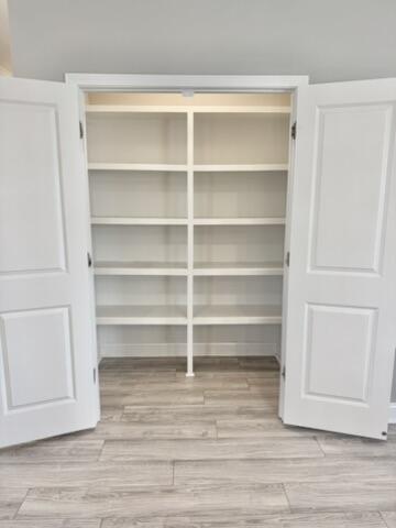 Open closet with built-in white shelves and wood-look plank flooring.