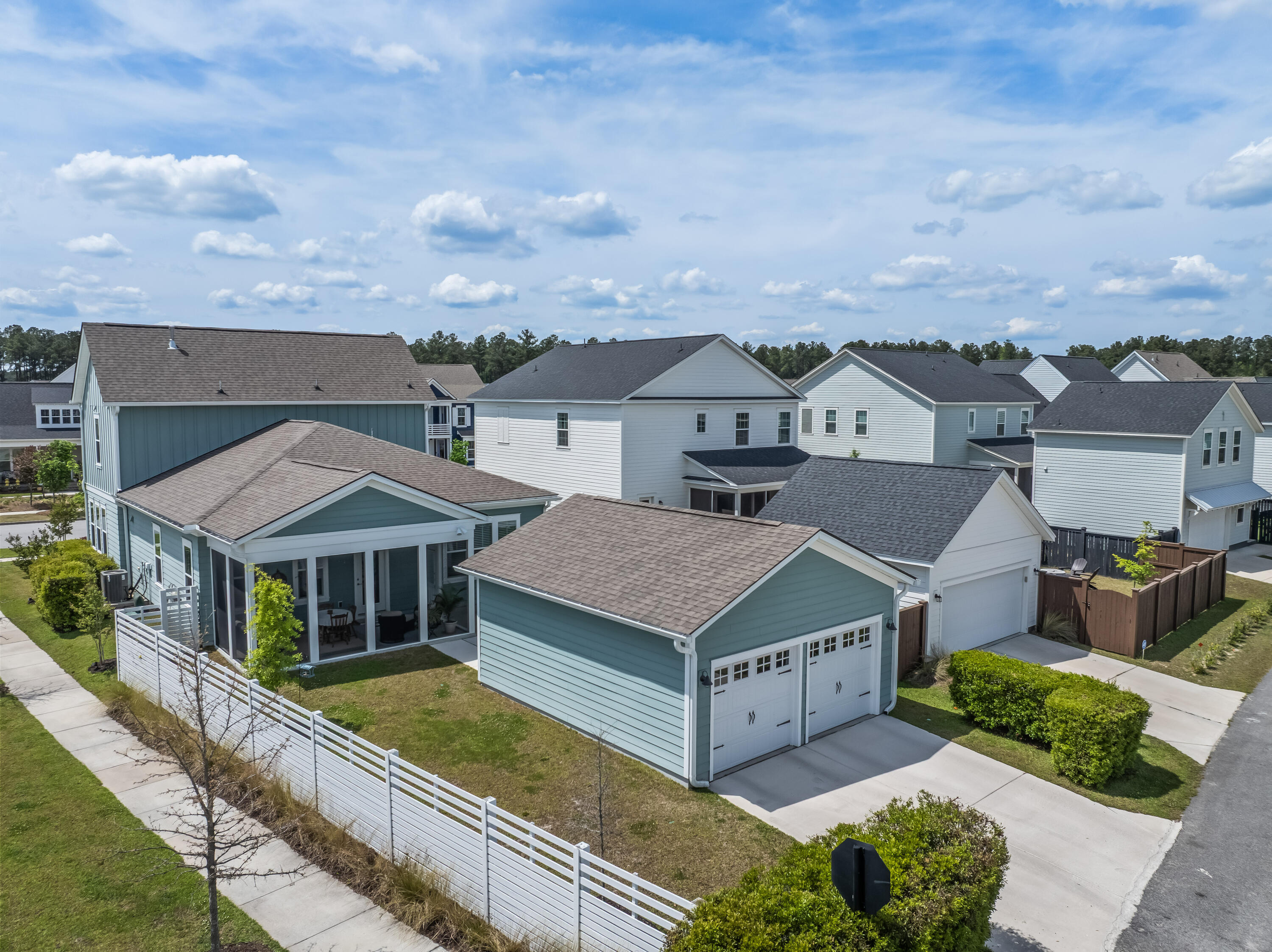 Aerial view of a blue-gray home with a screened porch, white fence, and garage.