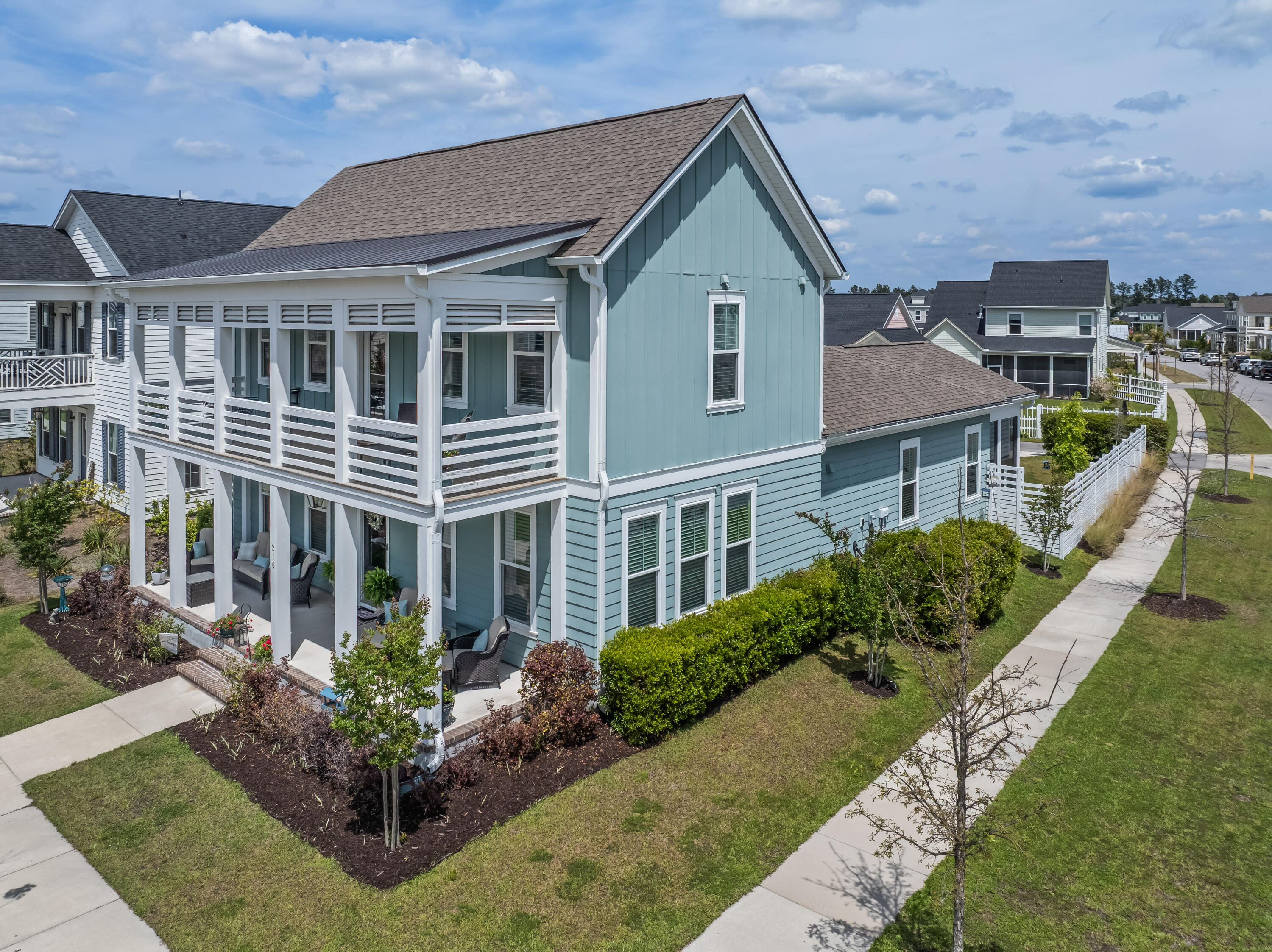 Blue-gray two-story house with a covered patio and upper balcony, seen from above on a landscaped corner lot.