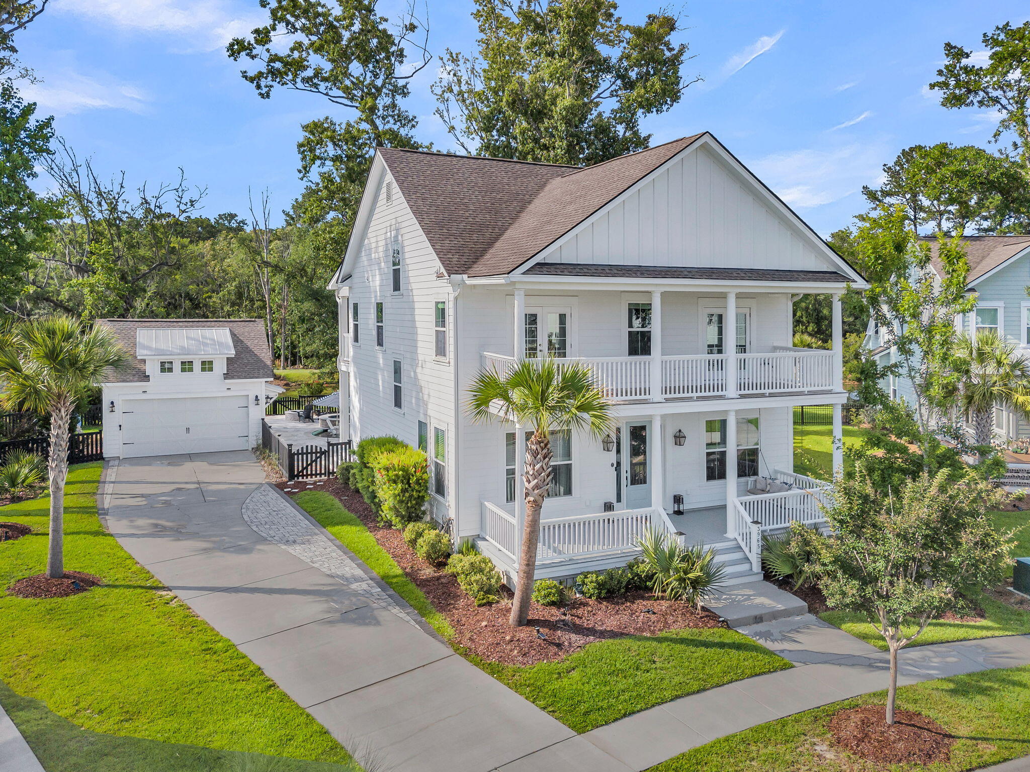 White two-story house with covered porches, detached garage, palm trees, and curved driveway.