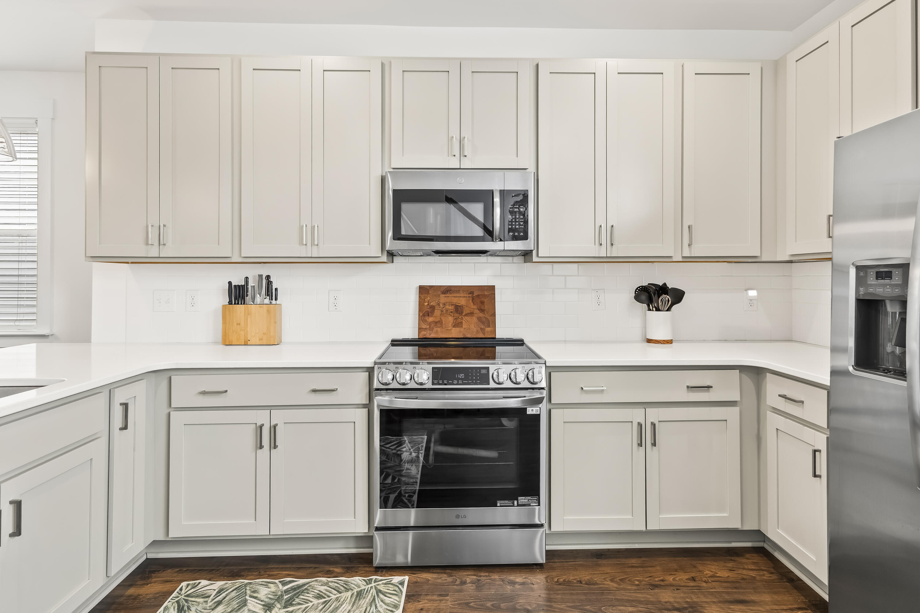Bright kitchen with white shaker cabinets, stainless steel appliances, and dark wood flooring.