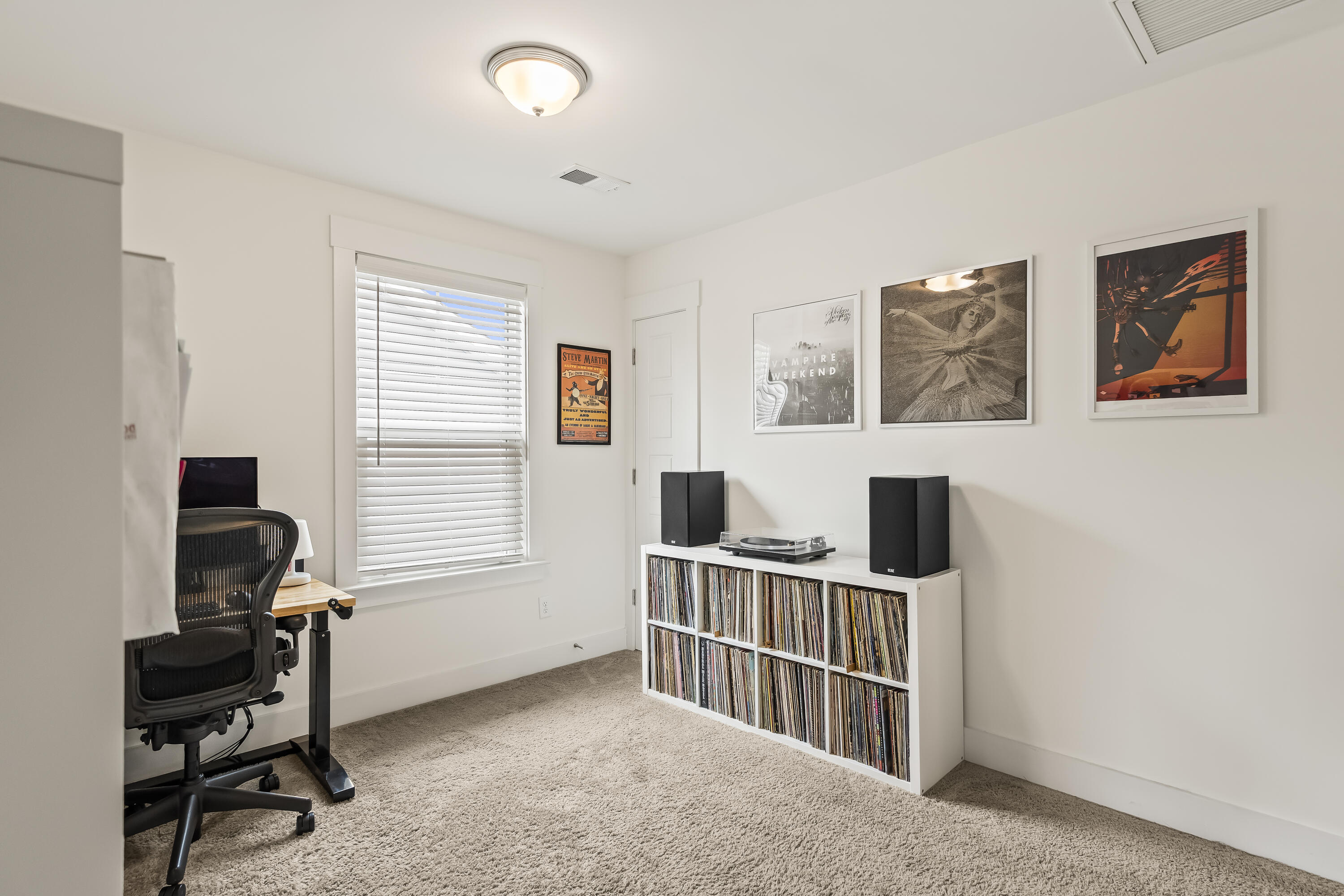 Home office with a record cabinet, turntable, speakers, framed posters, and a desk by the window.