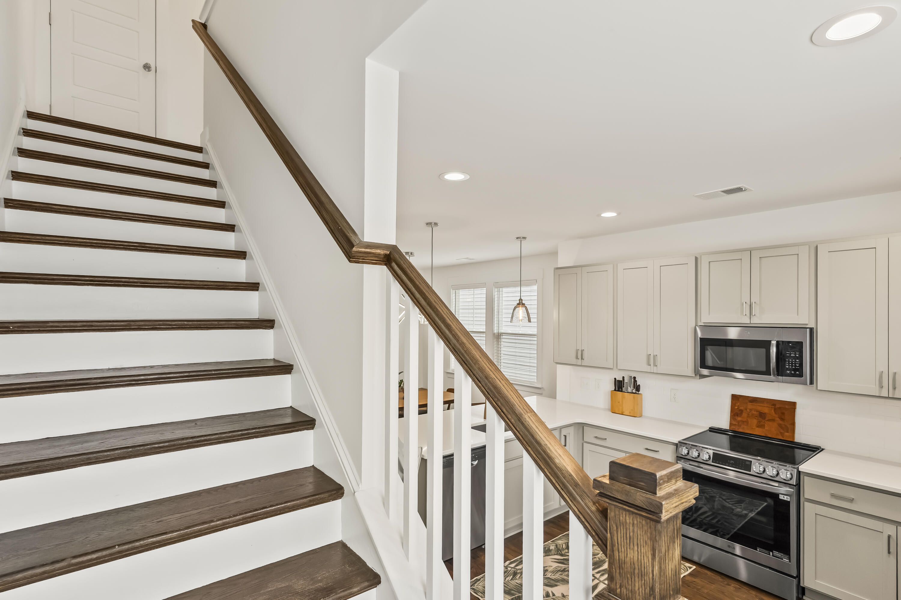 White kitchen beside a staircase with dark wood treads and handrail.