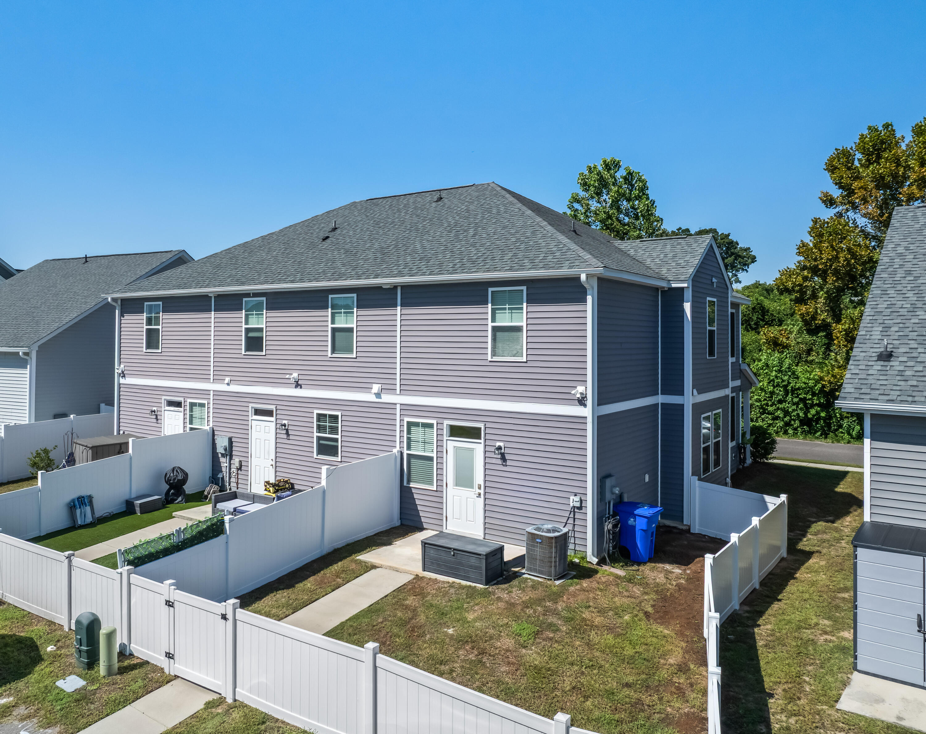 Rear of a two-story gray-sided home with white-fenced yards and multiple rear entrances.