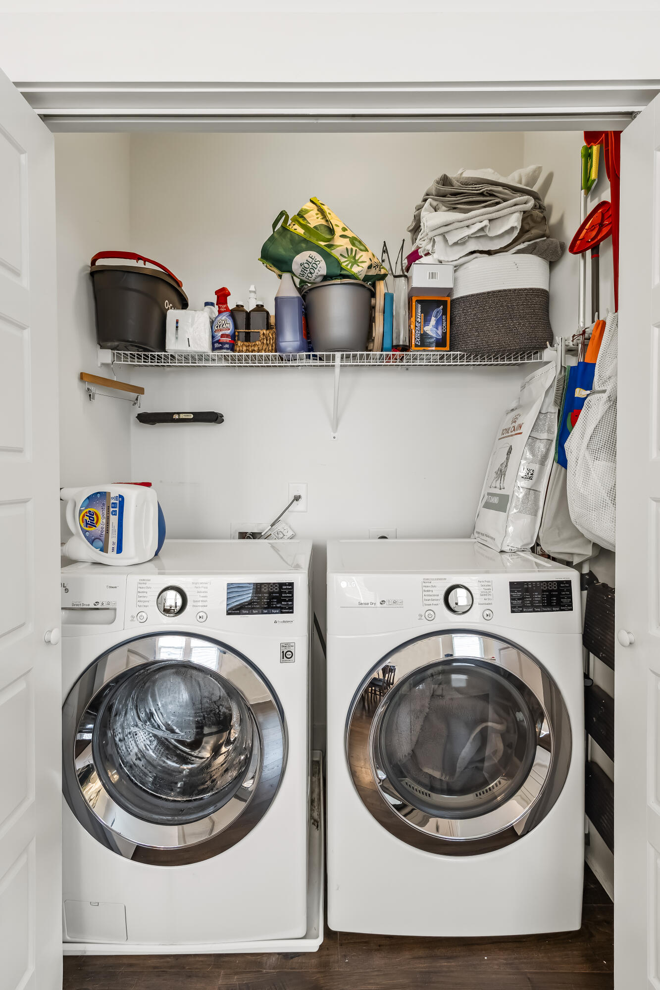 Laundry room with white front-loading washer and dryer beneath a storage shelf.