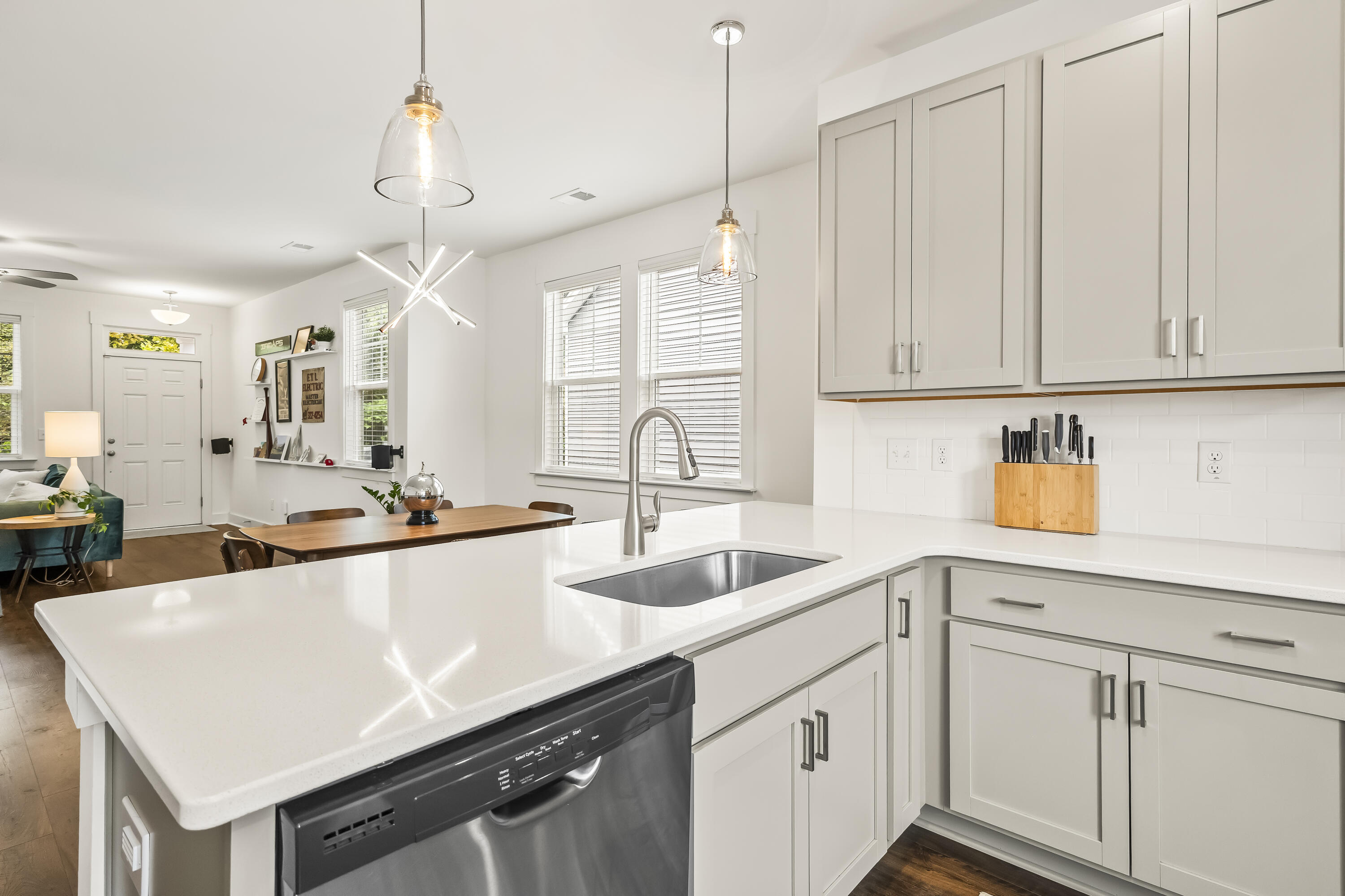 Bright white kitchen with a large peninsula, undermount sink, stainless dishwasher, and open dining area.