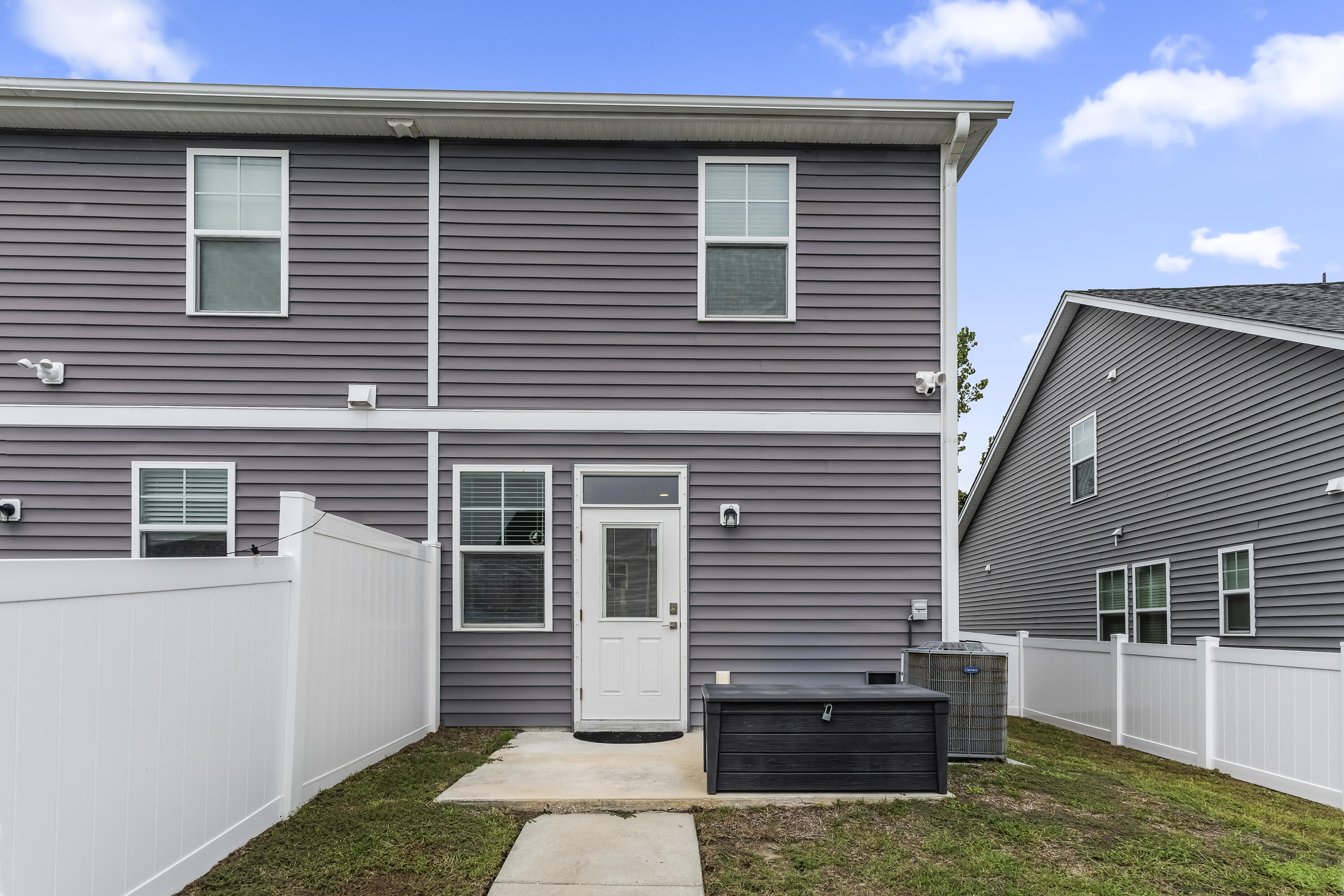 Rear of a gray two-story house with a fenced yard, concrete patio, and dark hot tub.