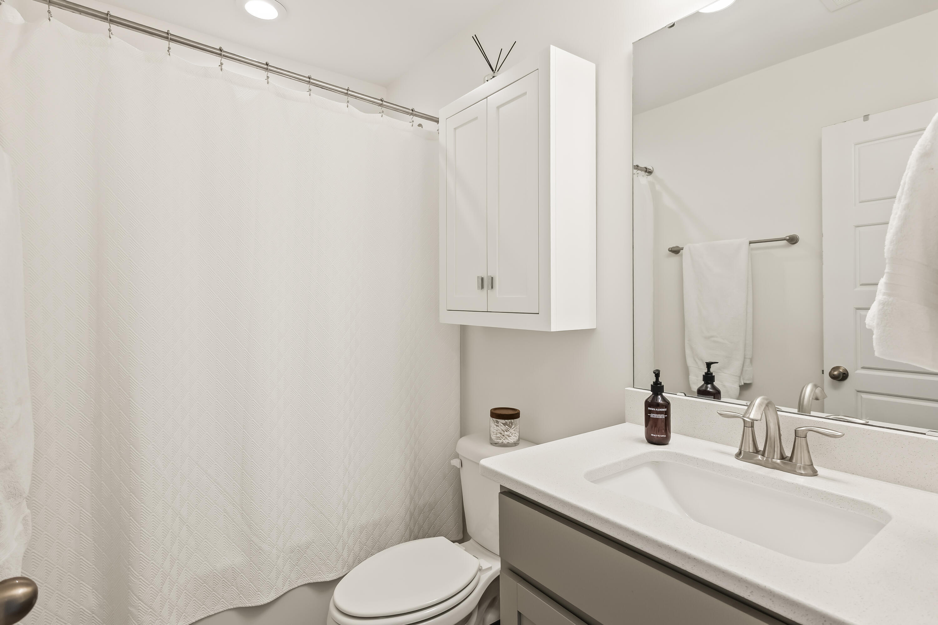 Bathroom with a patterned shower curtain, wall cabinet, toilet, and wide white vanity.