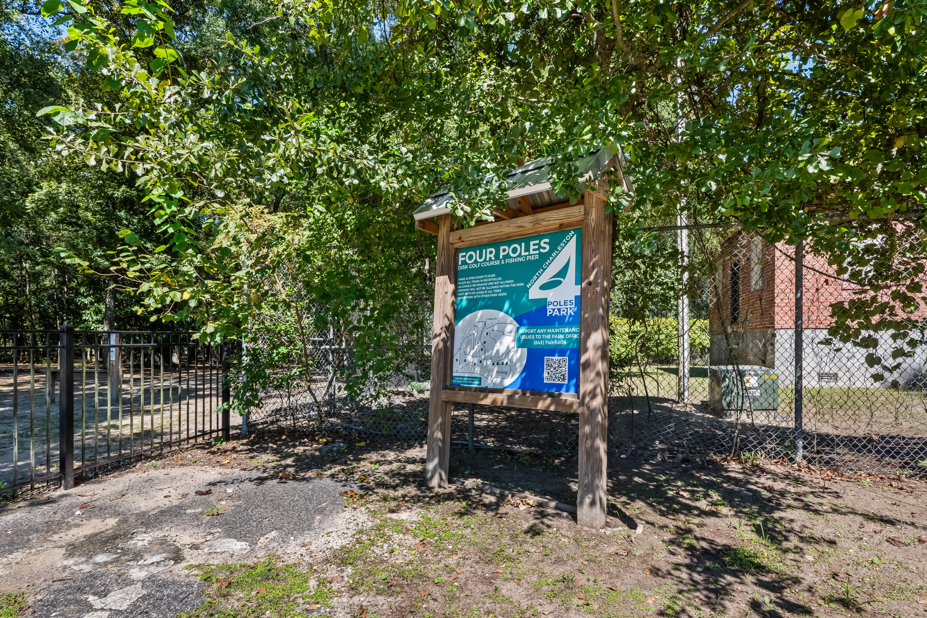 Four Poles Park entrance sign beneath trees beside a fenced park path.