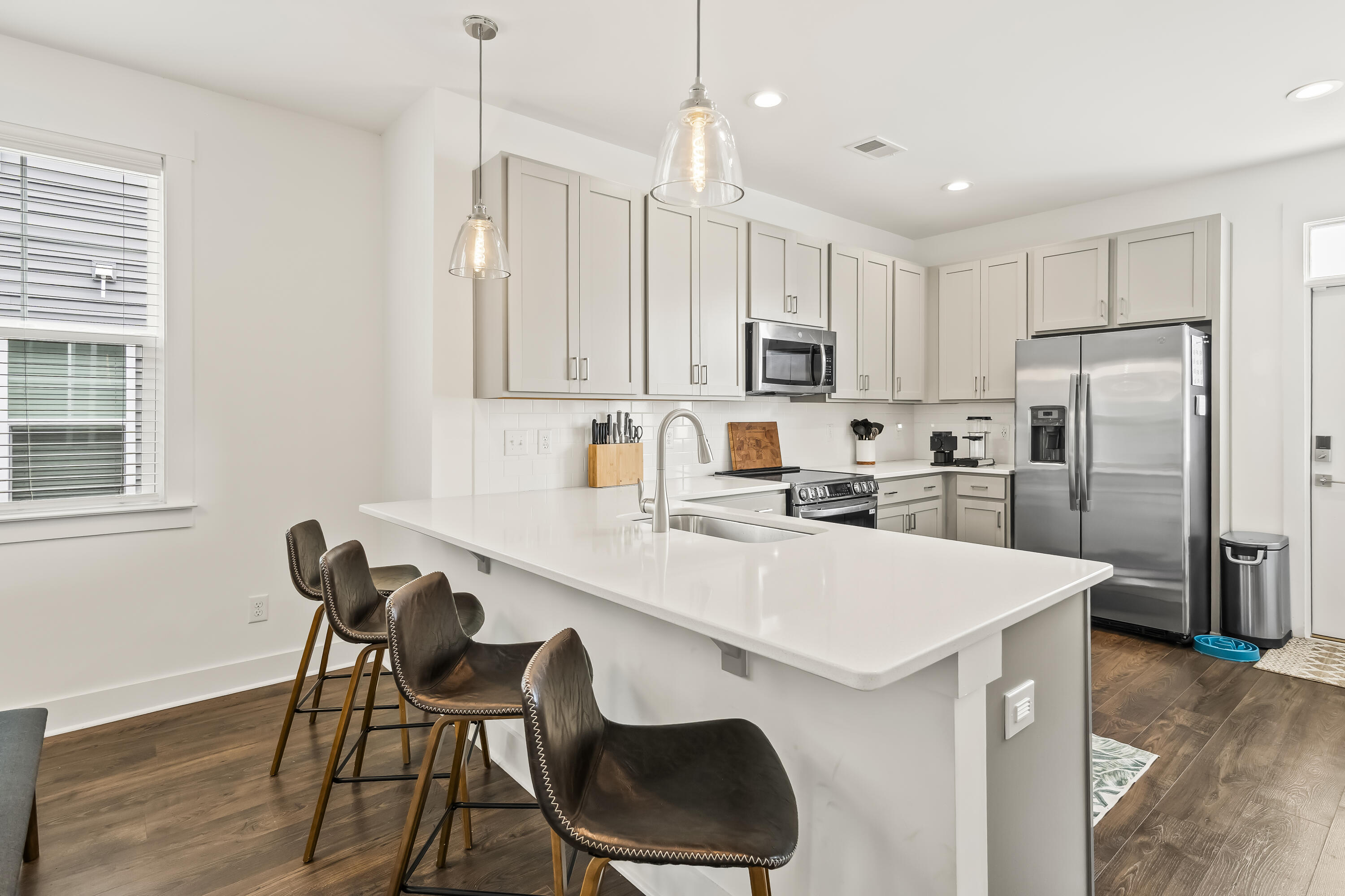 Modern kitchen with a large white island, four bar stools, and stainless steel appliances.