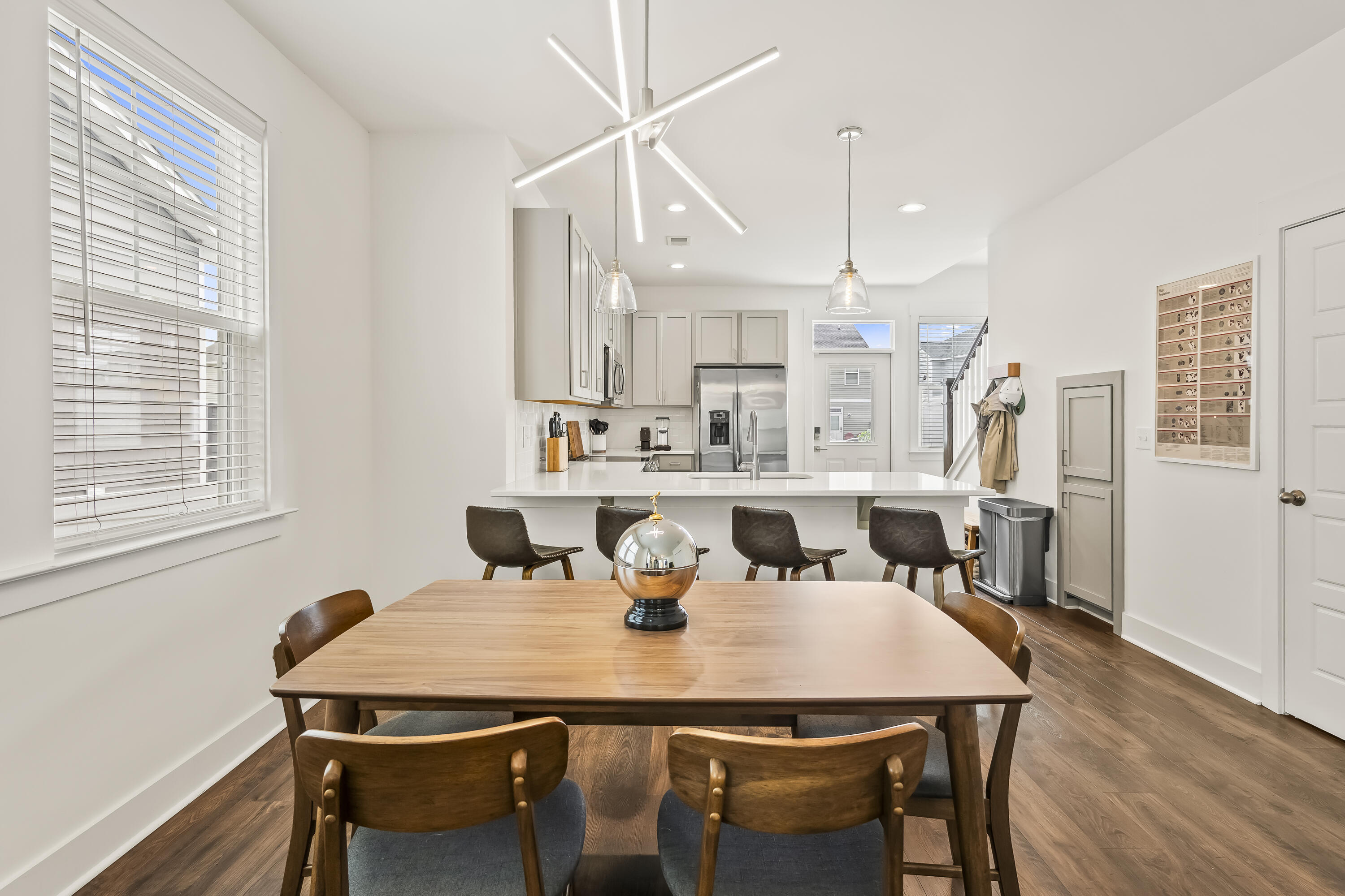 Dining area with a large wooden table opening onto a bright kitchen with white cabinets and stainless steel appliances.