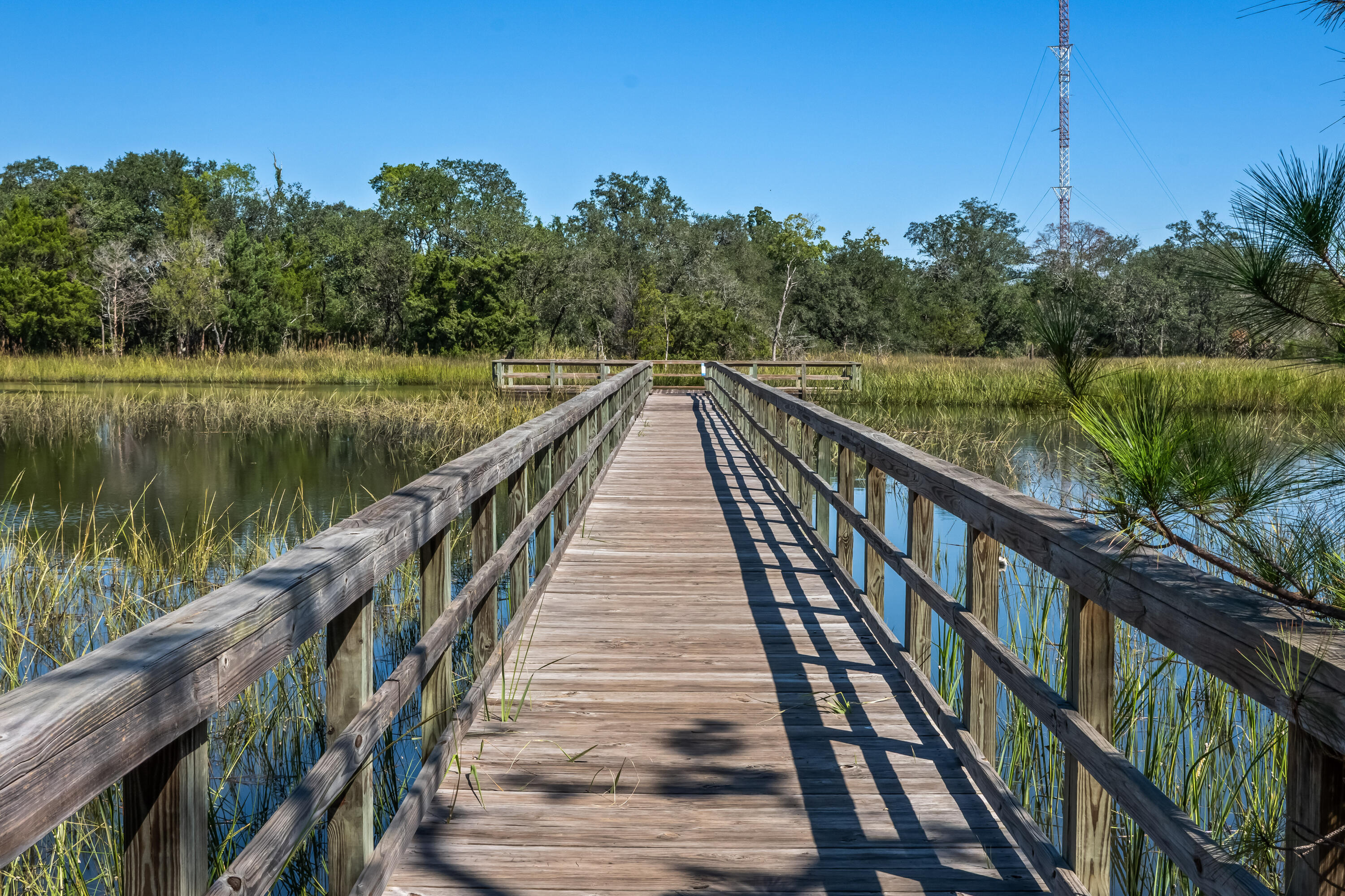 Wooden boardwalk crosses a marsh, with reeds, calm water, and a communications tower in the distance.