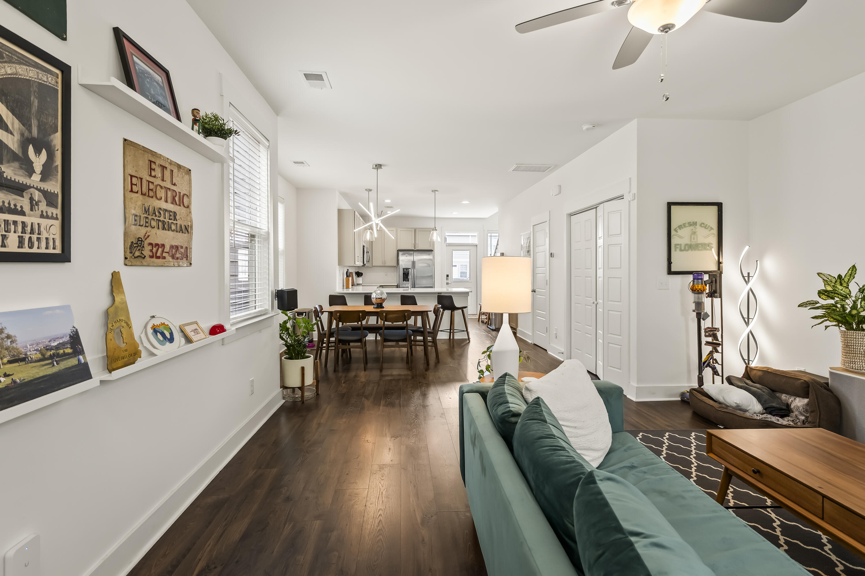 Open-plan living and dining area with a teal sofa, dark wood floors, and a kitchen beyond.