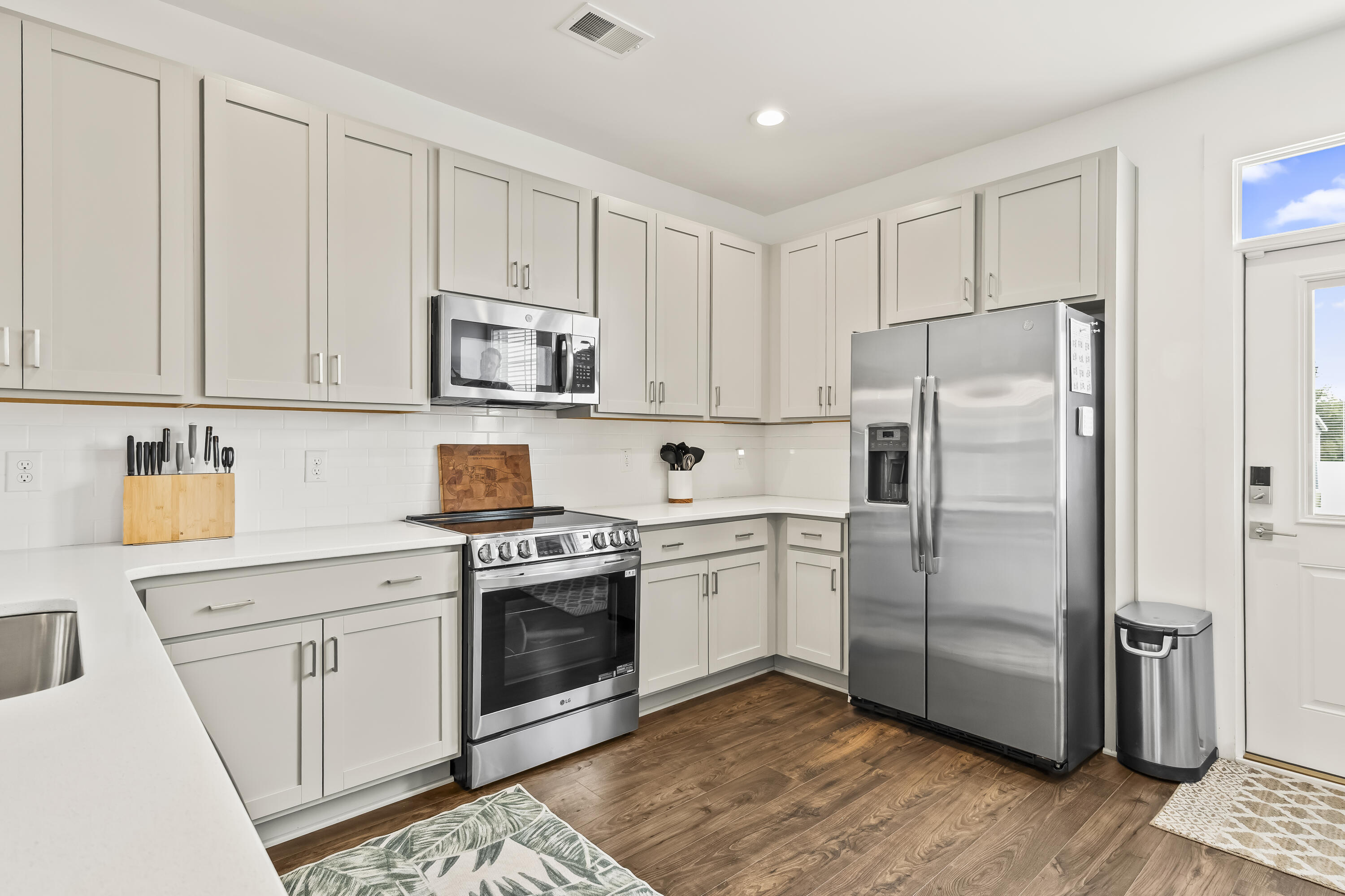 Kitchen with white cabinets, stainless steel appliances, and warm wood flooring.