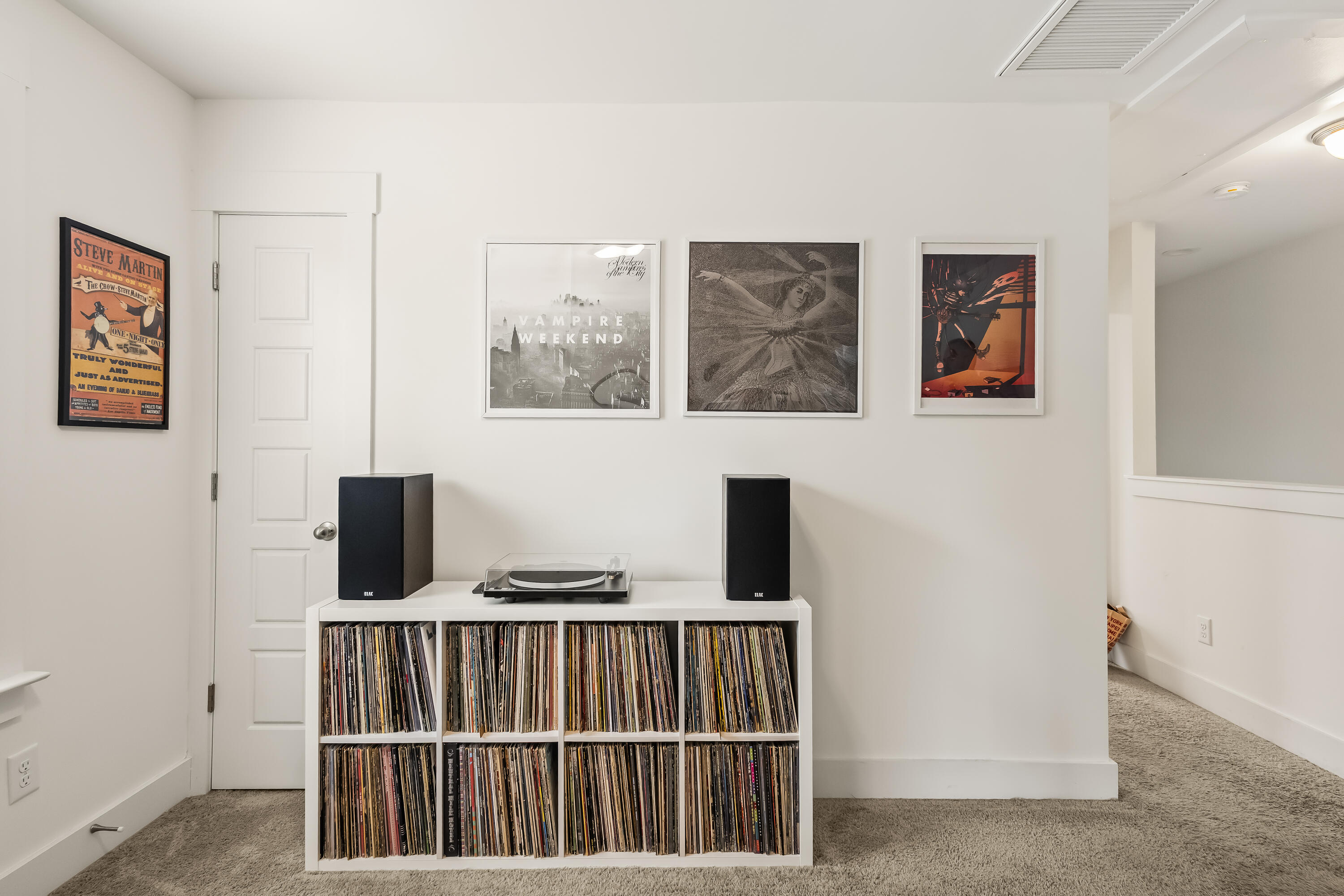 Music room with a turntable, speakers, and shelves of vinyl records beneath framed posters.