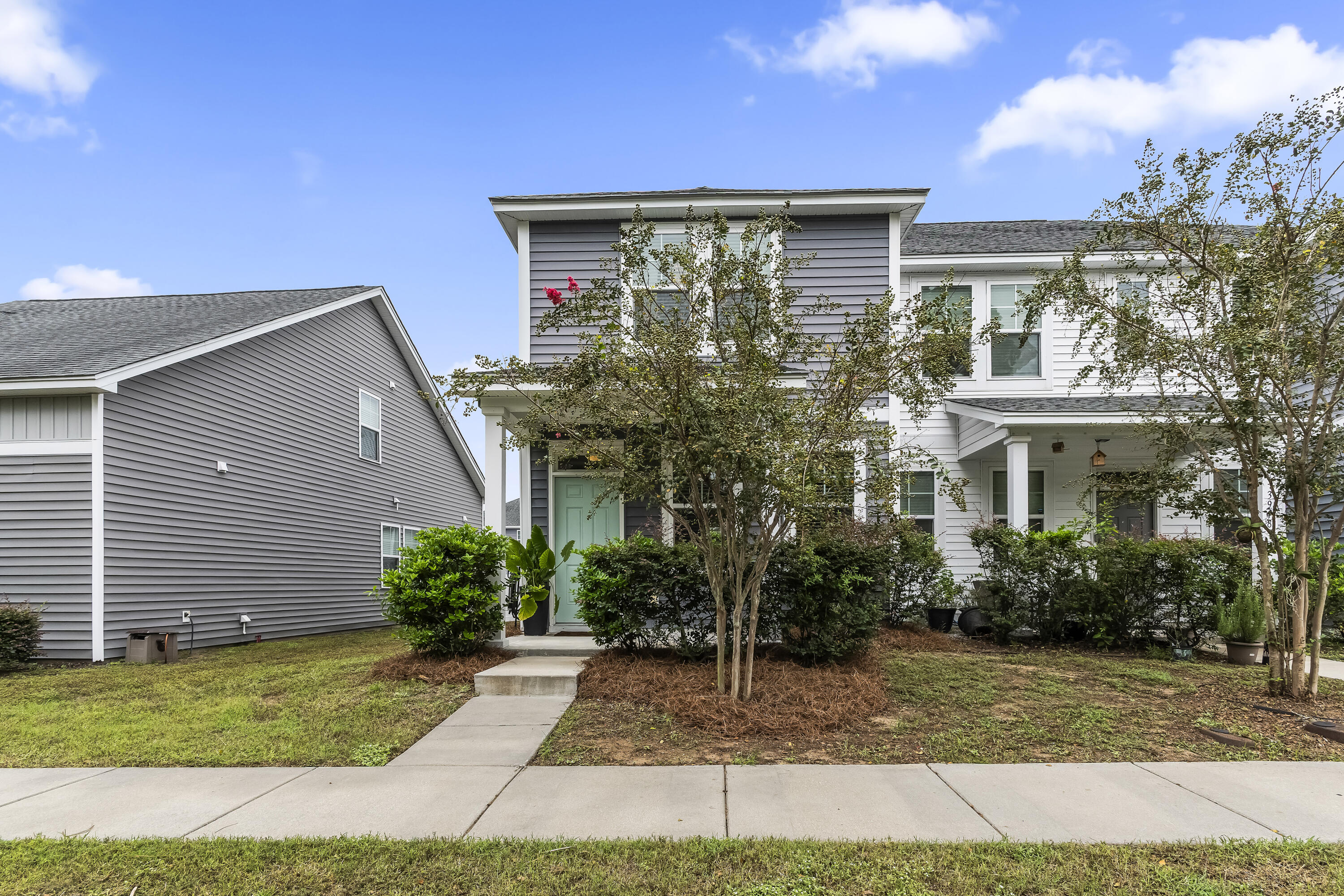 Two-story gray house with white trim, a pale green front door, and trees partly obscuring the façade.