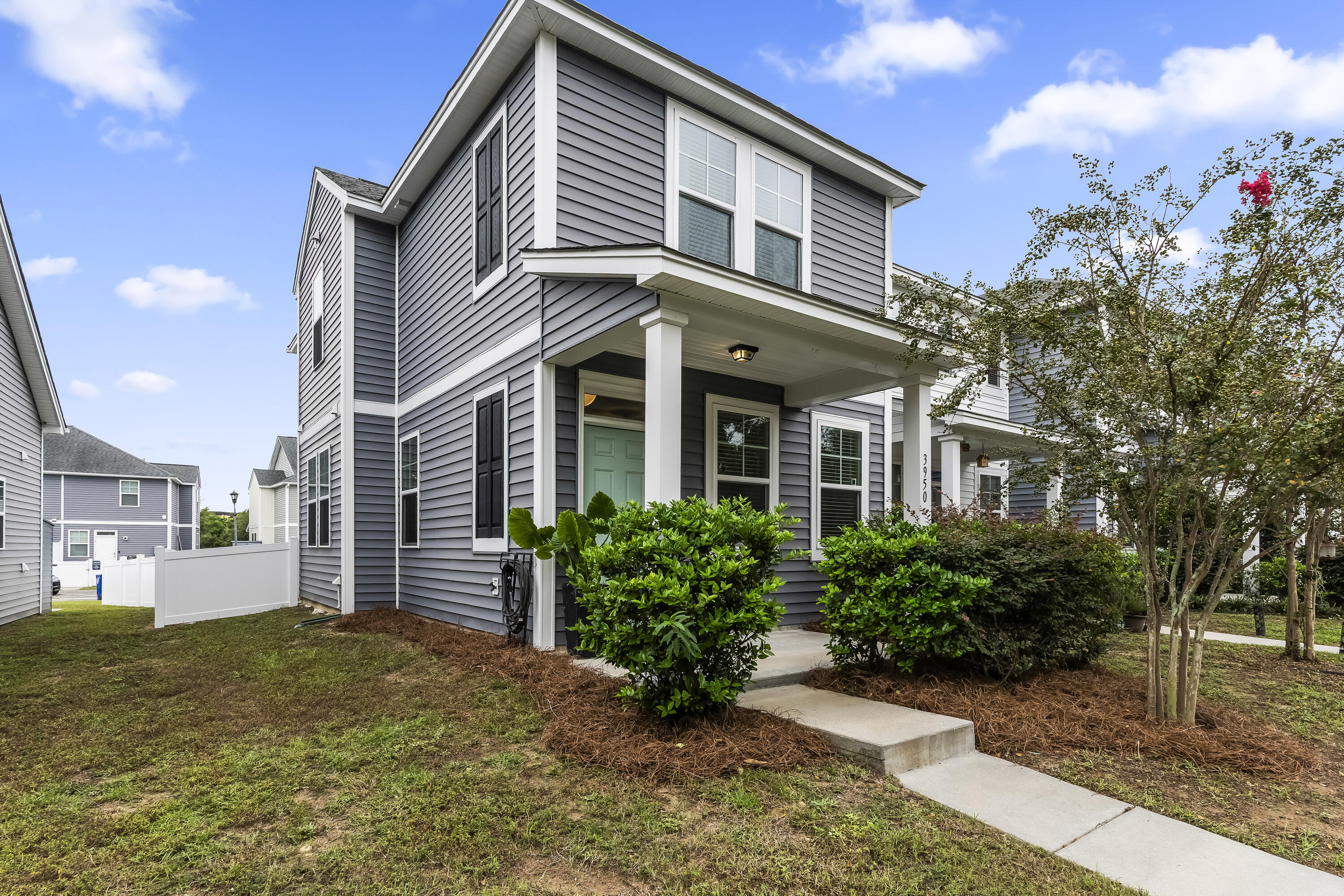 Two-story gray home with a covered porch, trimmed shrubs, and a concrete walkway to the entrance.