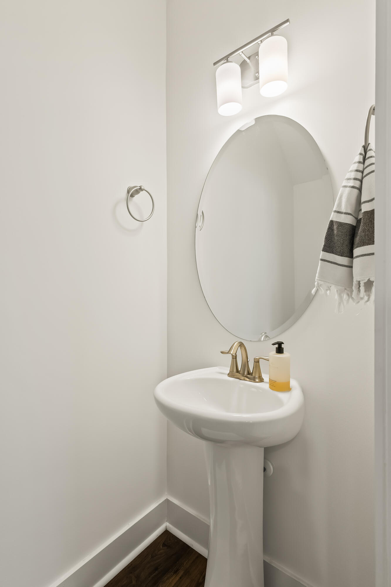 Bathroom pedestal sink with brass-toned faucet beneath an oval mirror and striped towel.